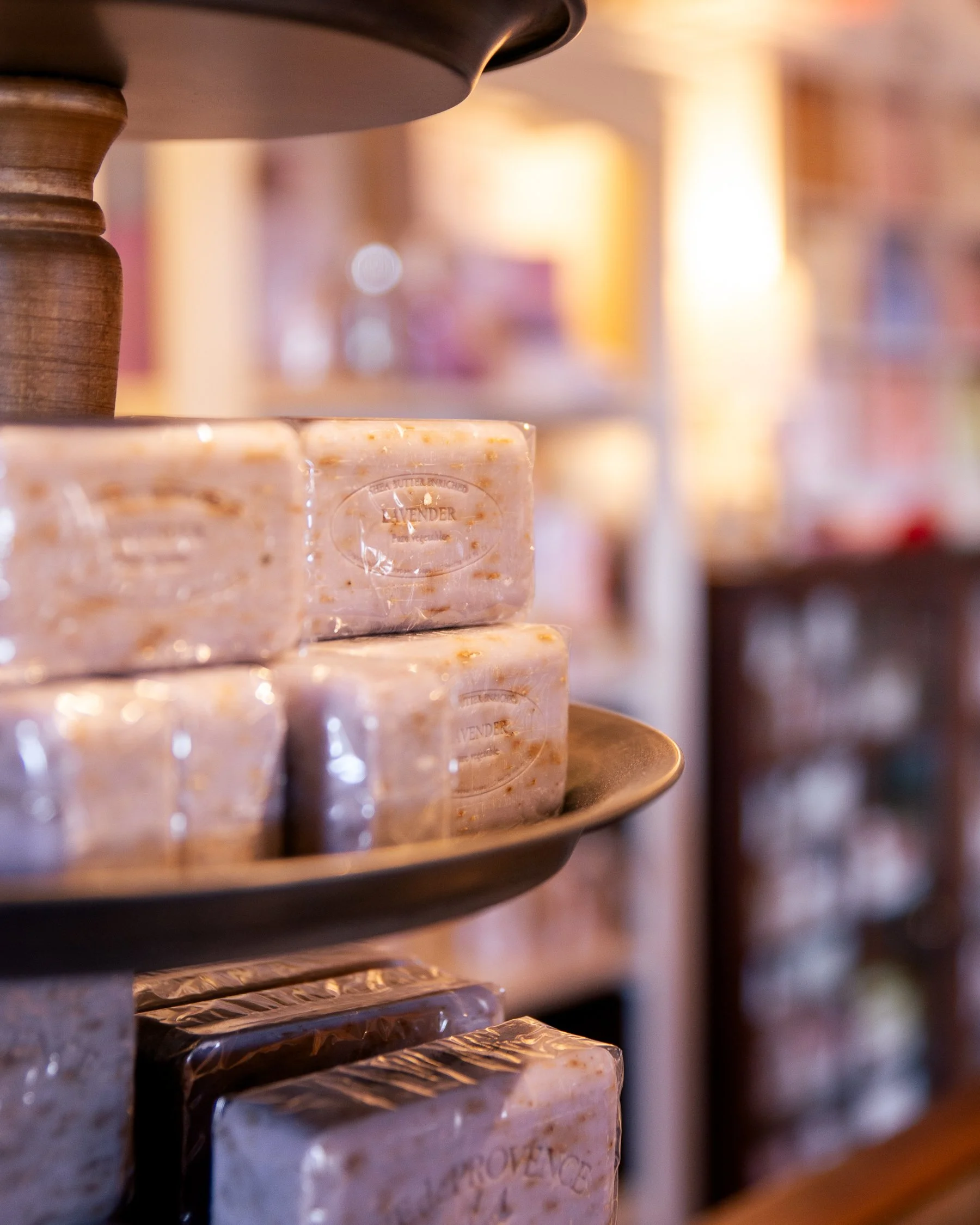 Stacked bars of soap labeled 'Lavender' on a display shelf in a soap shop with warm light
