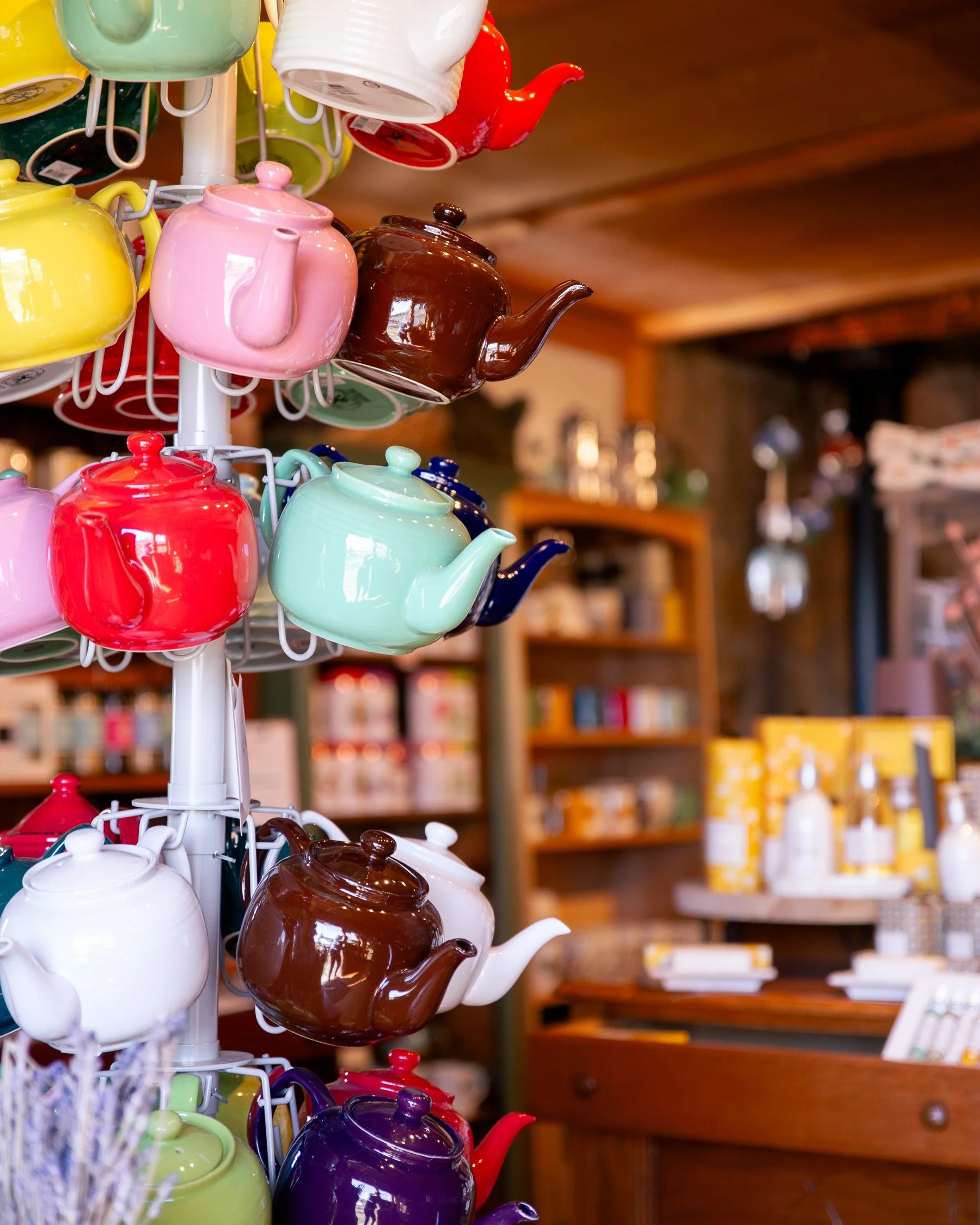 Colorful teapots hanging on a display rack inside a store with rustic wooden ceiling