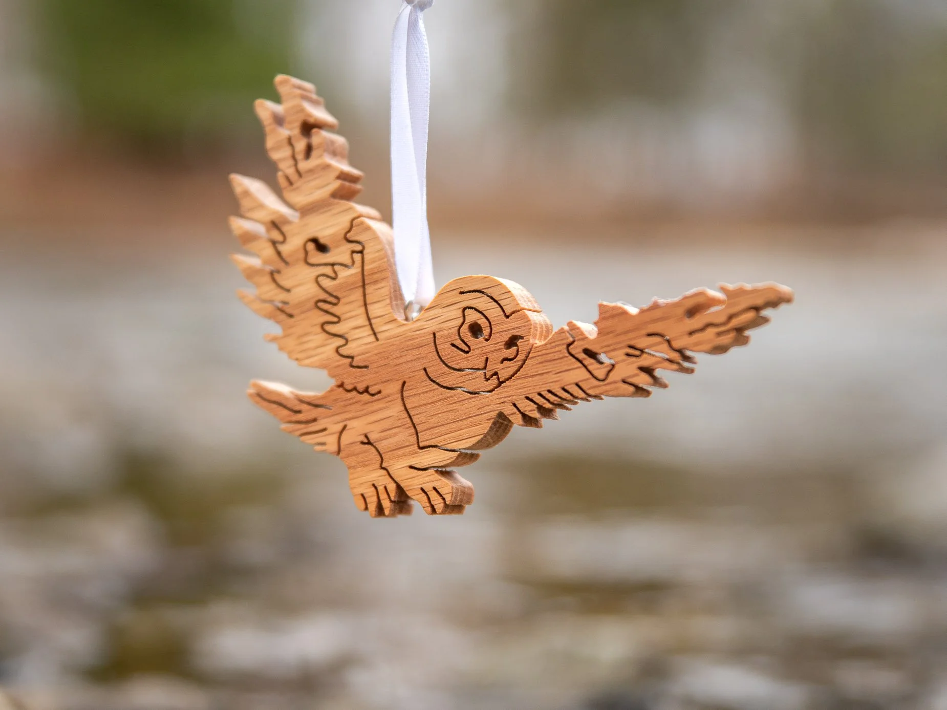 A wooden ornament in the shape of an owl with wings spread and outlines of Manitoulin Island, hanging from a white ribbon over a river