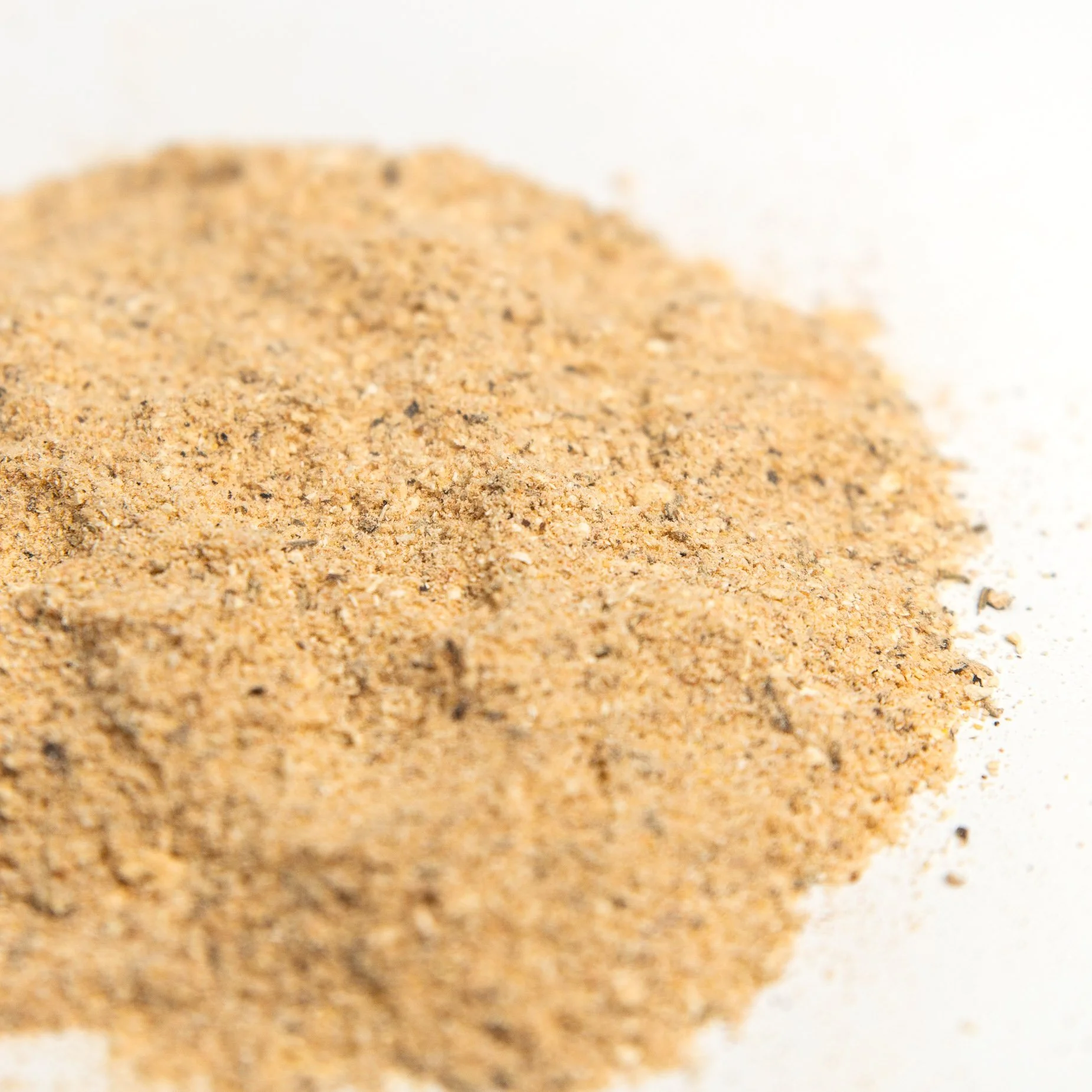 Close-up of light brown ground mushroom spice from Heartwood Mushrooms with tiny darker specks, scattered on a white surface.