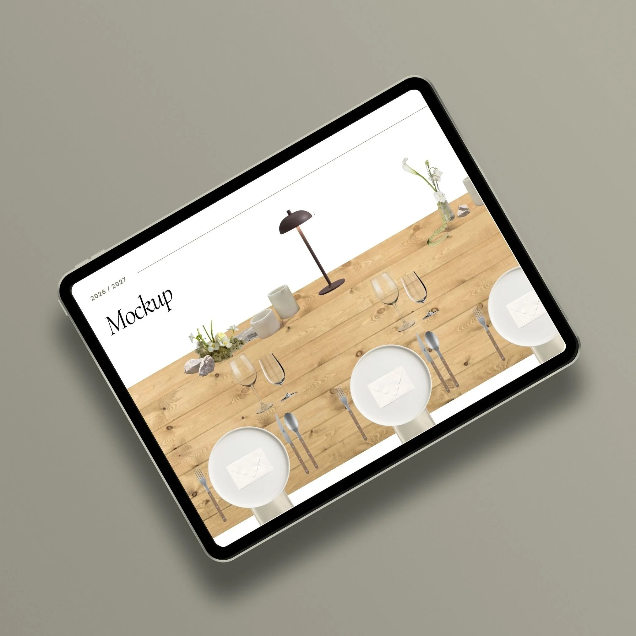Tablet displaying a mockup of a table setting with candles, vases, wine glasses, and plates on a wooden table, with the word 'Mockup' and date 2026/2027 in the corner.