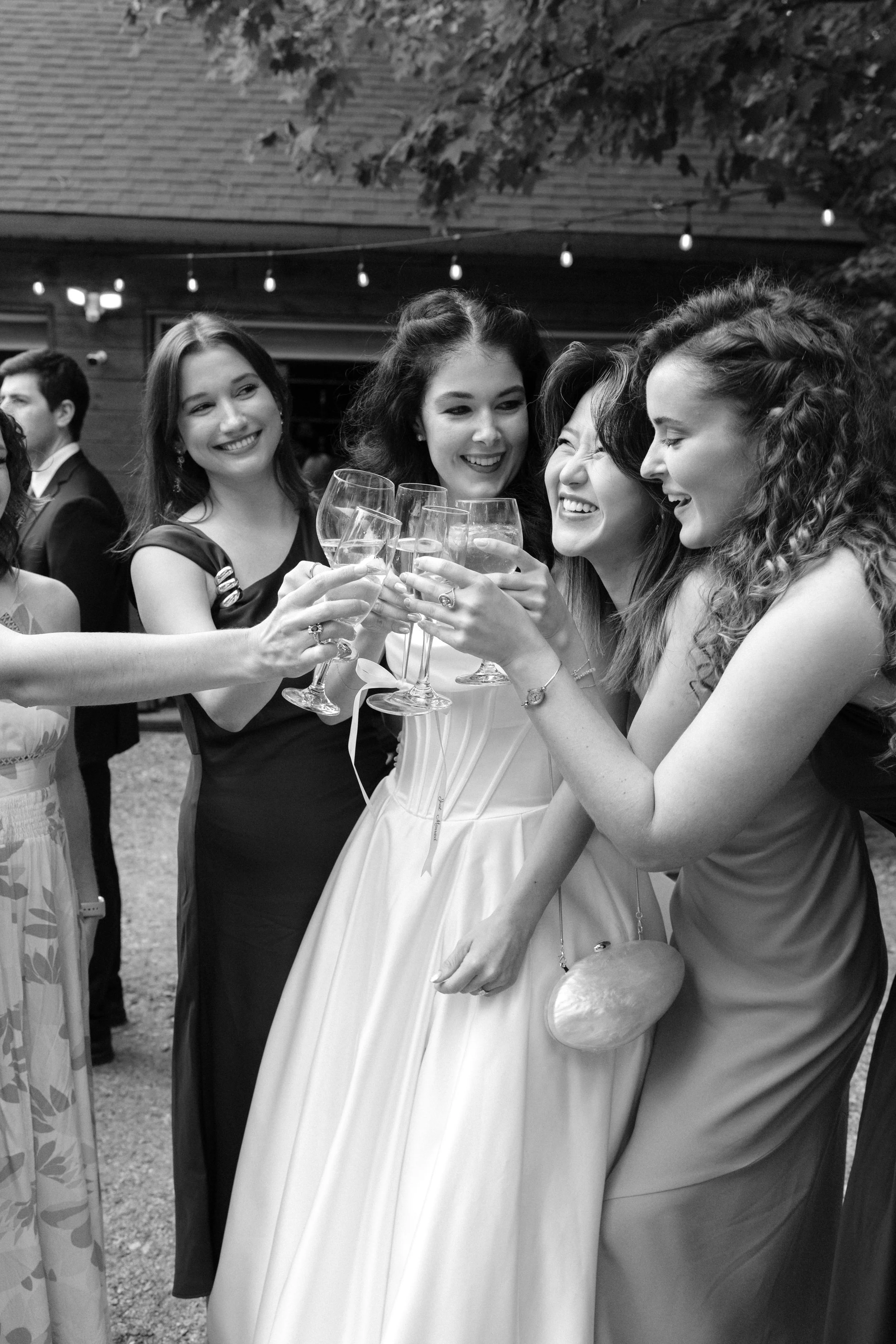A group of women celebrating with champagne glasses at an outdoor party or wedding reception, smiling and toasting together.