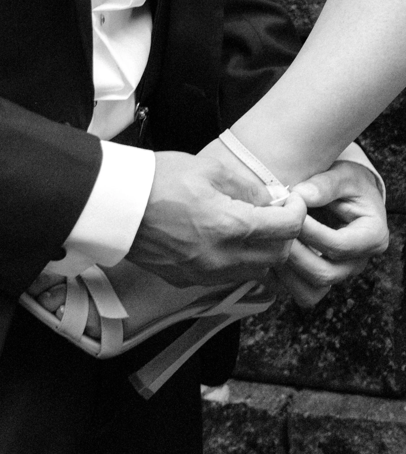 A person in a formal suit is adjusting the strap of a sandal on someone's foot.