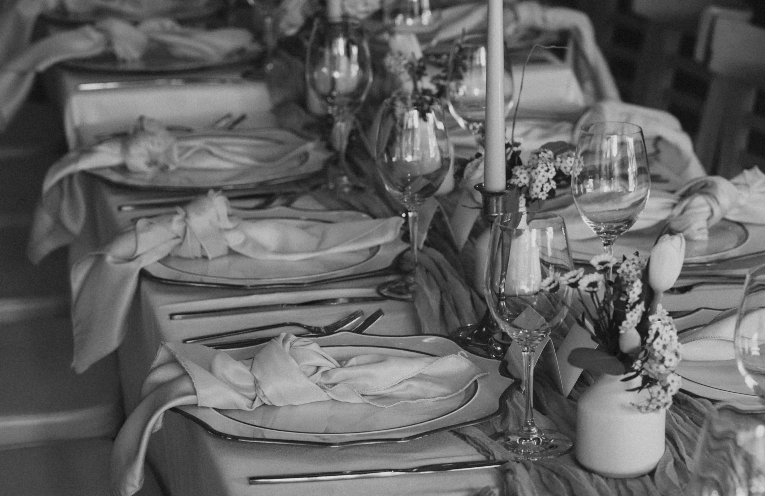 Elegant table setting with napkins, glasses, a candle, and floral arrangements for a formal event.