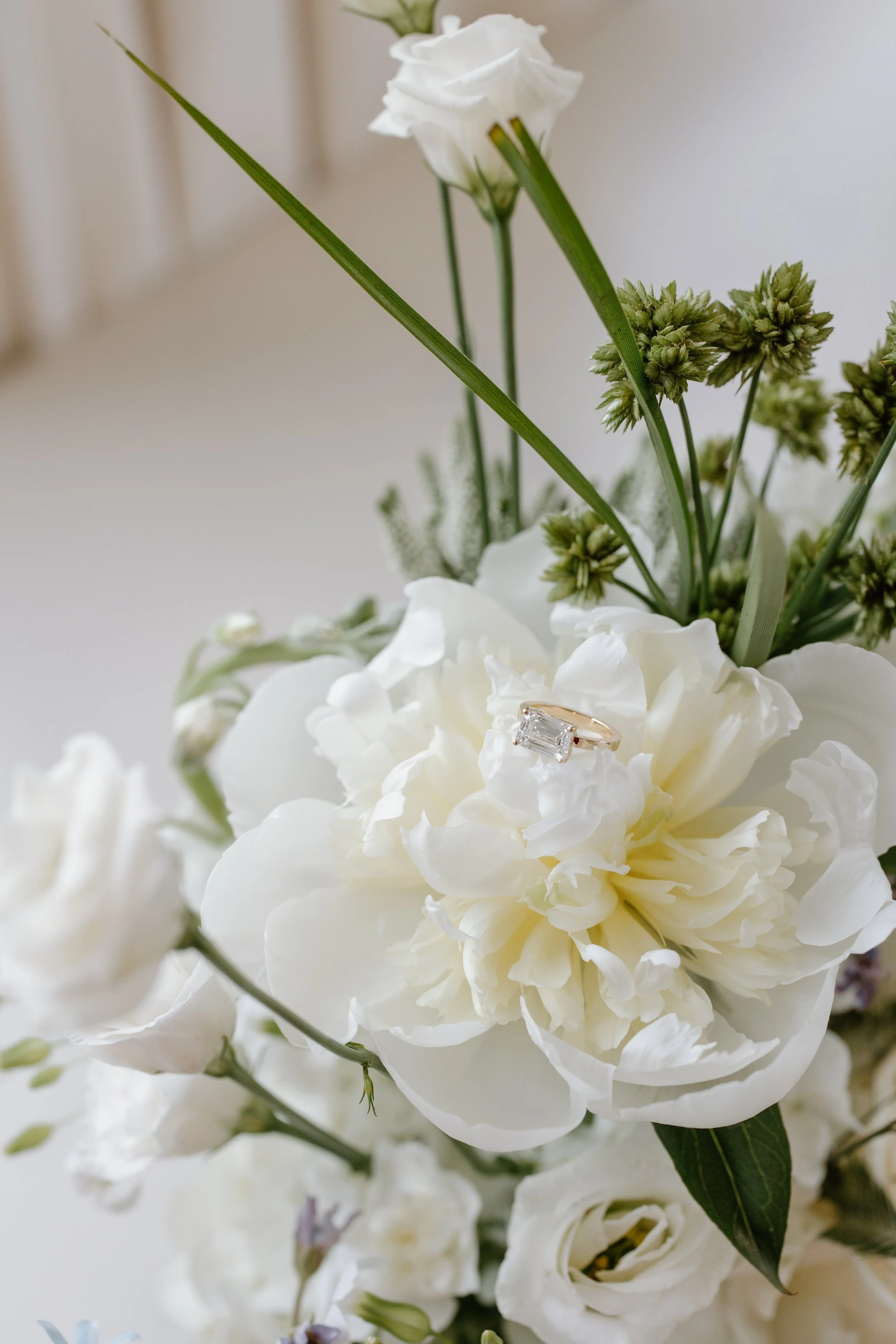 A close-up of a white floral arrangement with a diamond ring resting on a large white flower.