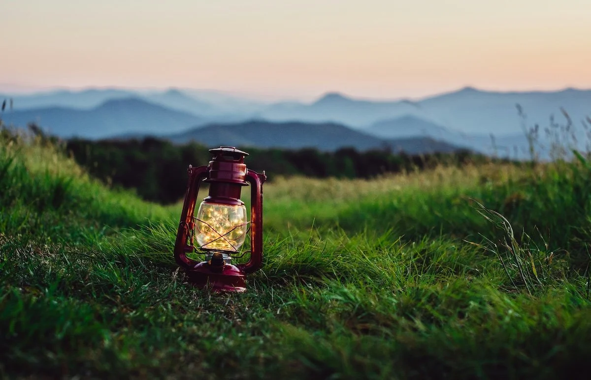 An old-fashioned red lantern sits on green grass, with the Tennessee mountains in the background.