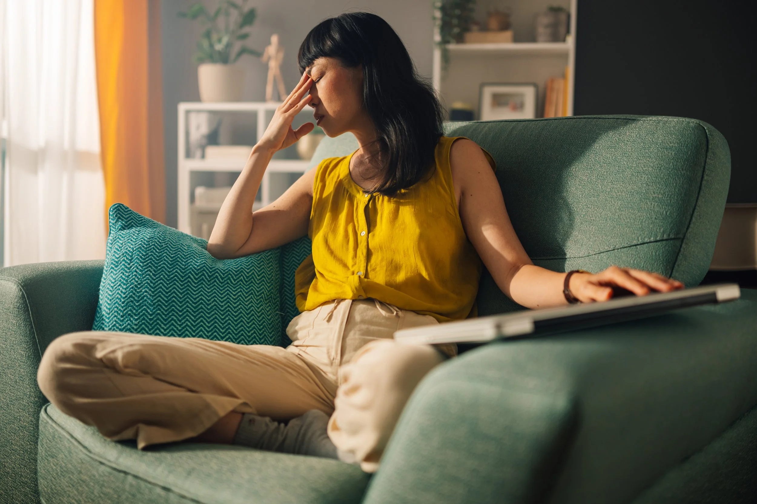 A woman in a mustard yellow shirt sits in a comfy therapy chair with her laptop closed