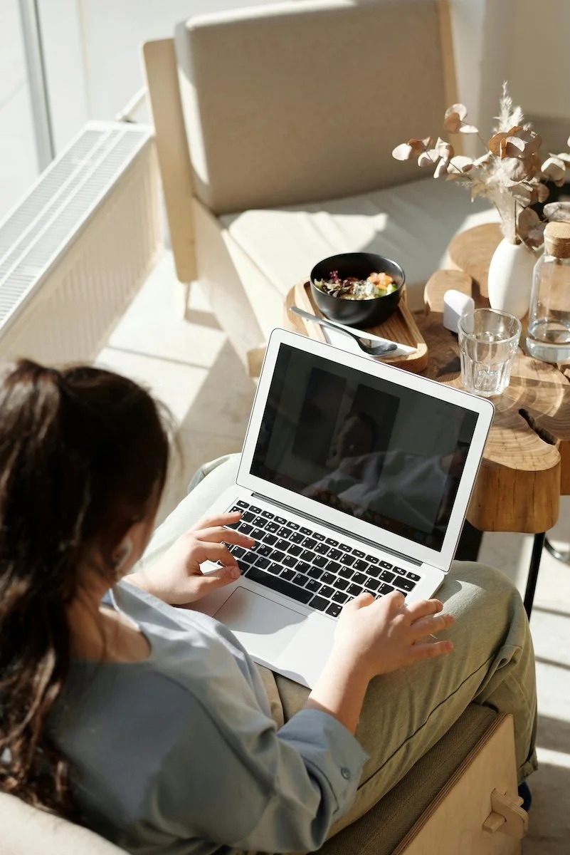 A woman with dark hair sits in her living room, logged into her online therapy session.