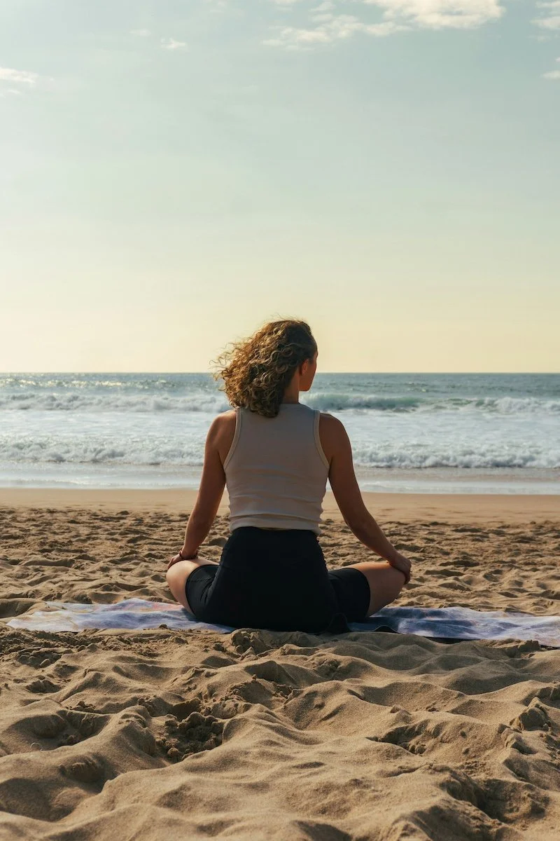 A woman with curly hair meditates on the sand at Rehobeth Beach, Delaware.