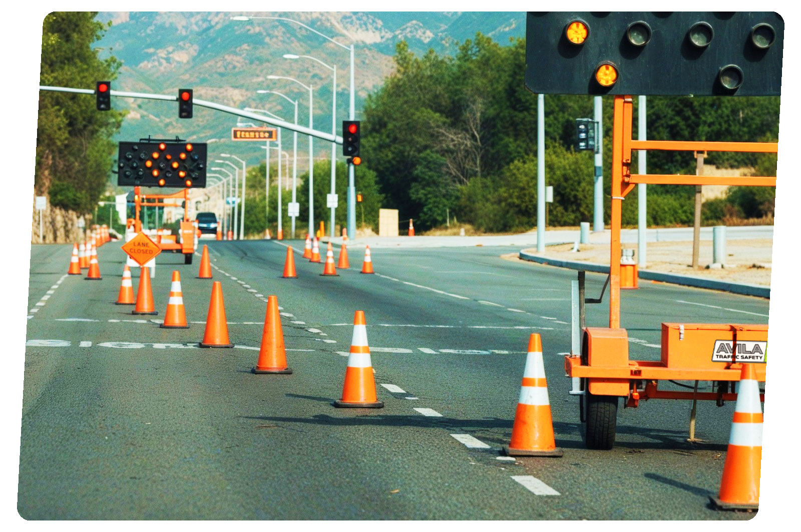 A highway lane closed for construction, with orange traffic cones, electronic signals showing red lights, and a sign that says 'Lane Closed'.