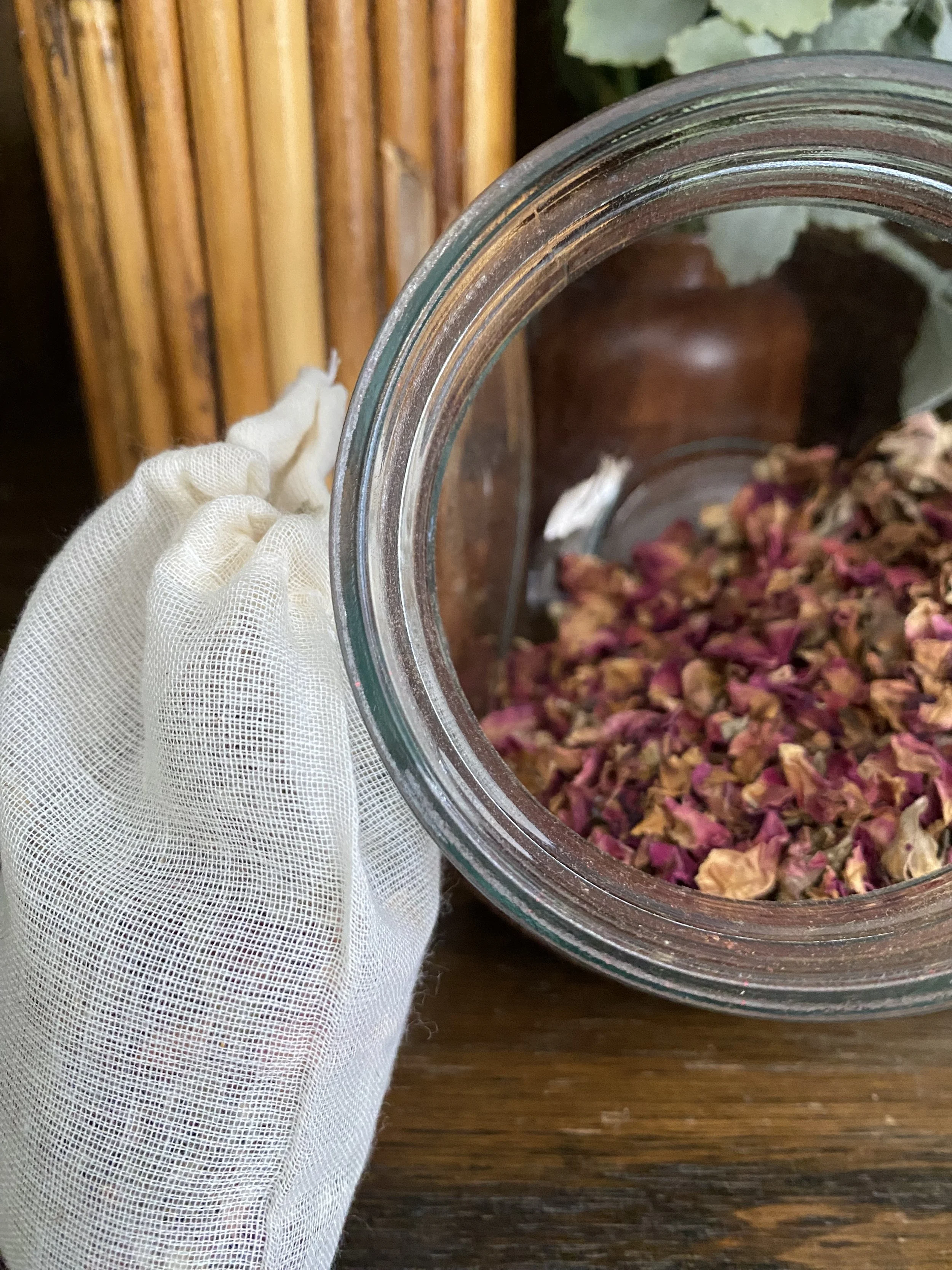 A hand wearing a white glove holding a glass jar with dried rose petals inside.
