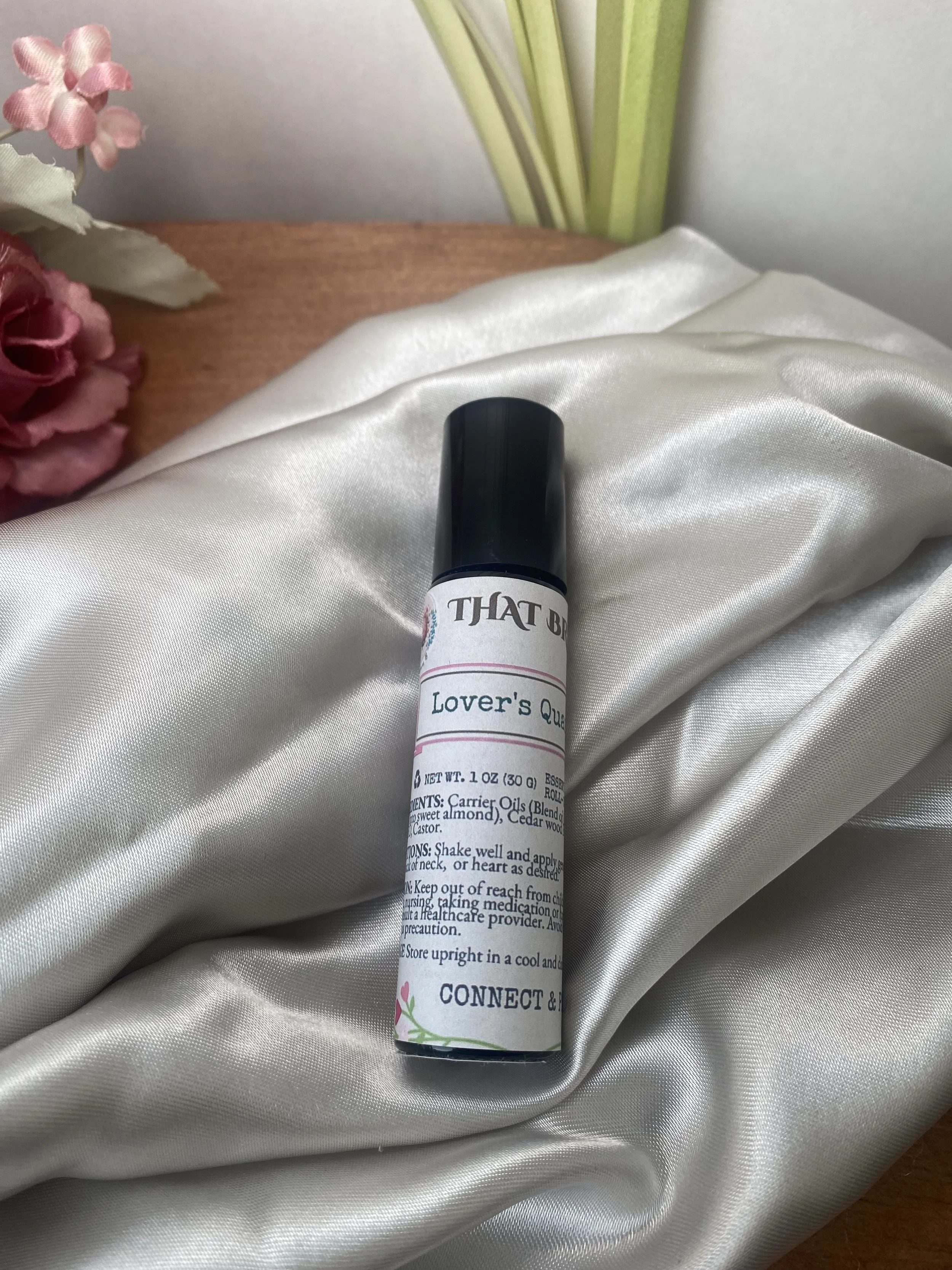 A white label roller on a satin fabric, with pink flowers and green leaves in the background.