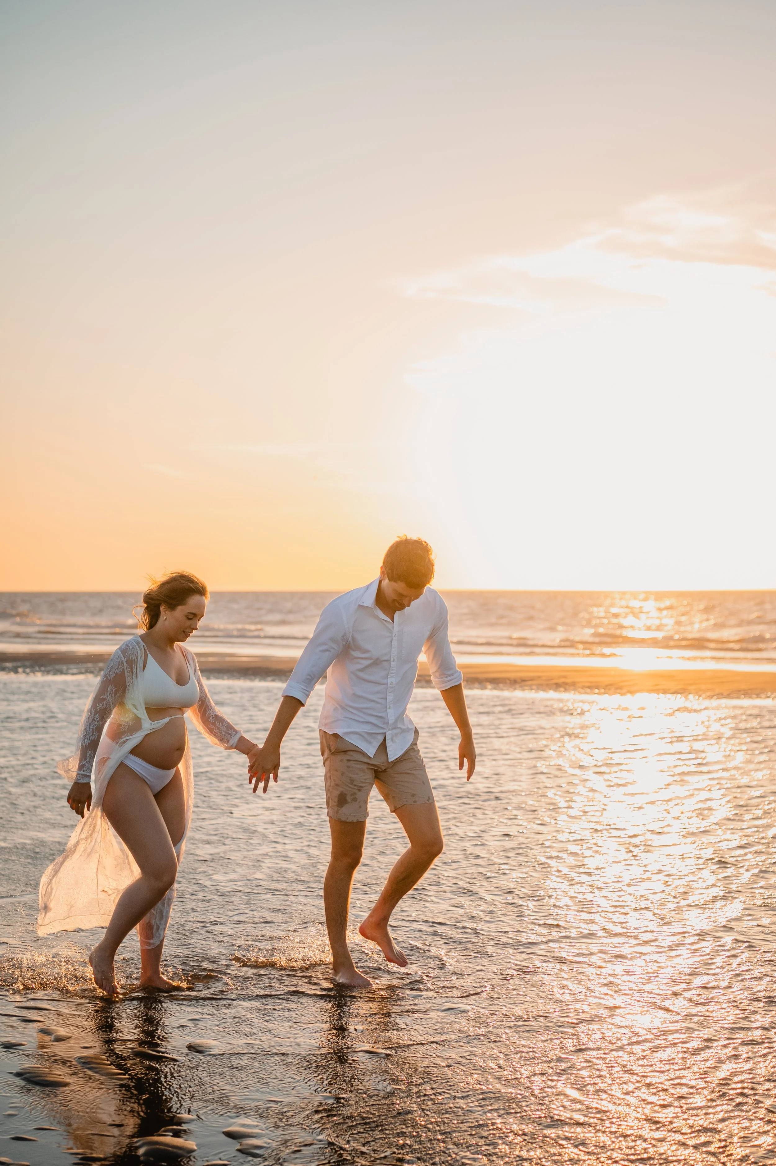 Een stel dat hand in hand op het strand wandelt tijdens zonsondergang, met de zee en een heldere lucht op de achtergrond.