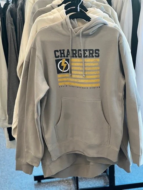 A beige hoodie with the San Diego Chargers logo and text on the front, hanging on a black hanger in a clothing store.