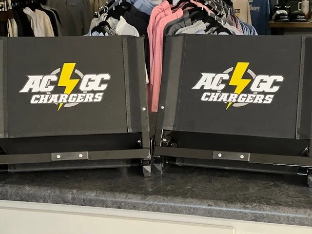 Two black AC Chargers retail display trays with yellow and white logo on a store counter.