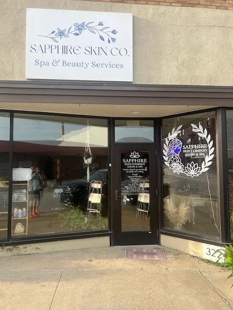 Front entrance of Sapphire Skin Co. Spa & Beauty Services with glass doors and windows, signboard above, and decorative window graphics.