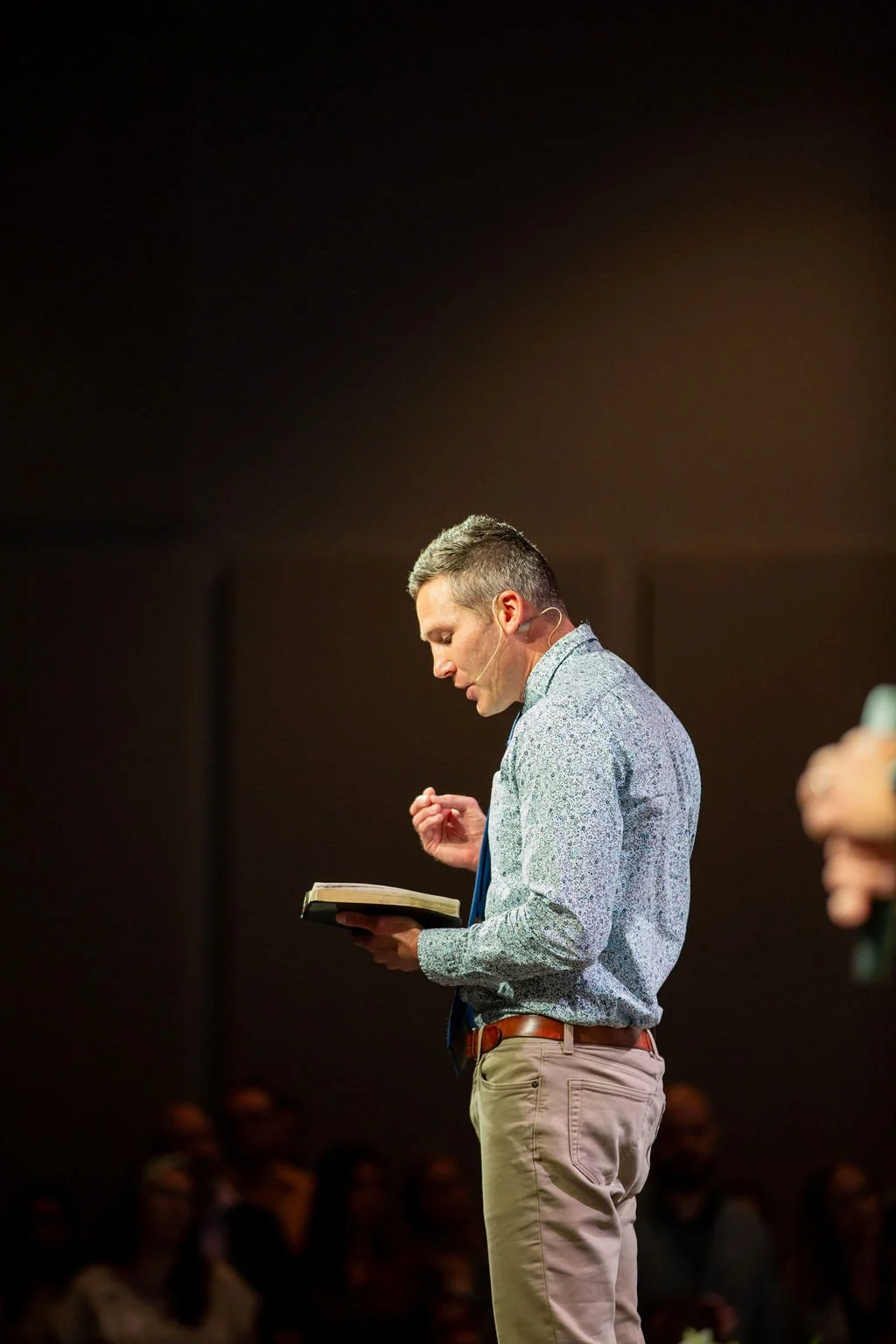 Pastor Chris Beals preaching in front of an illuminated cross at Pennington Park Church in Fishers, IN