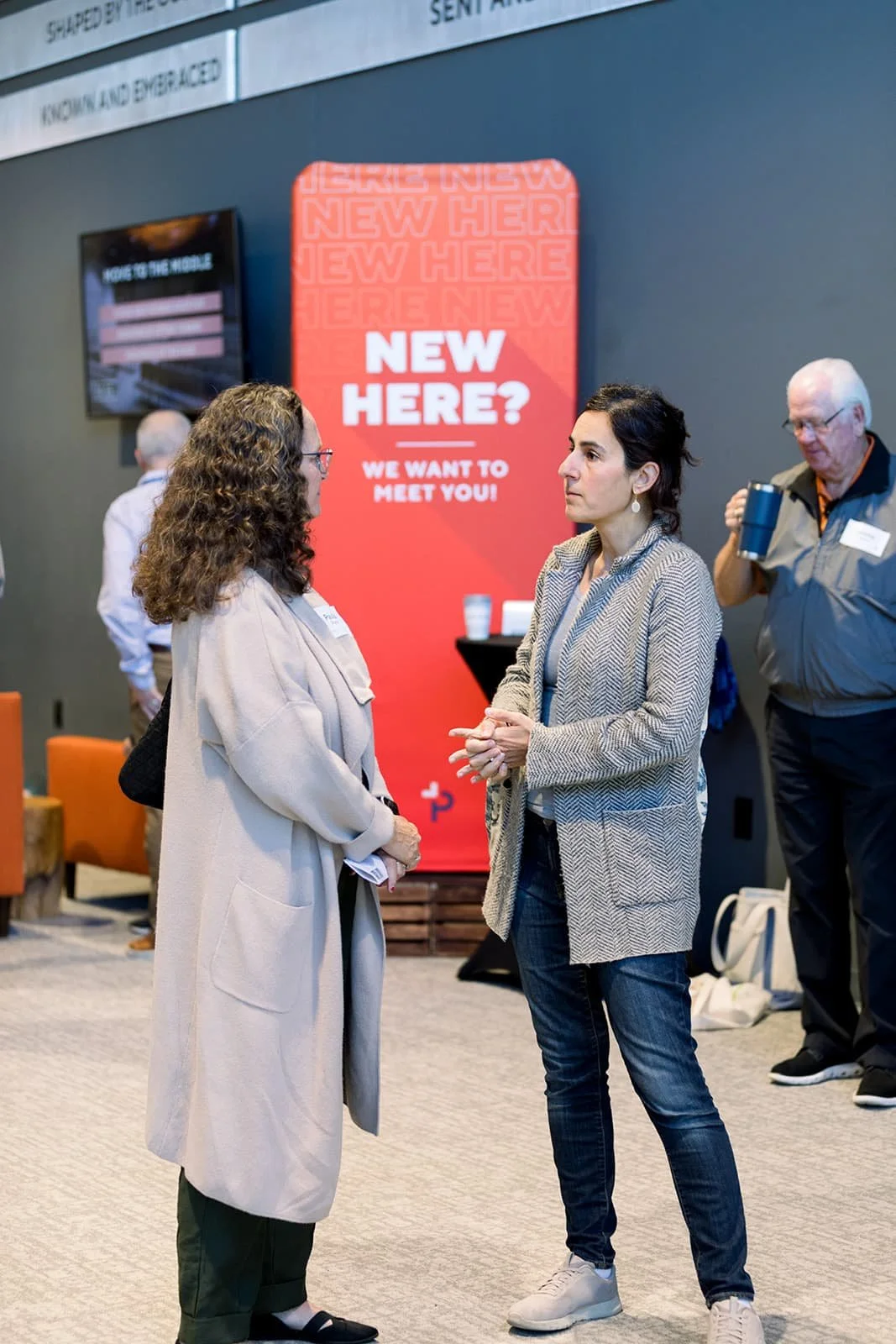 two women conversing in front of a New Here banner in the lobby at Pennington Park Church in Fishers, IN