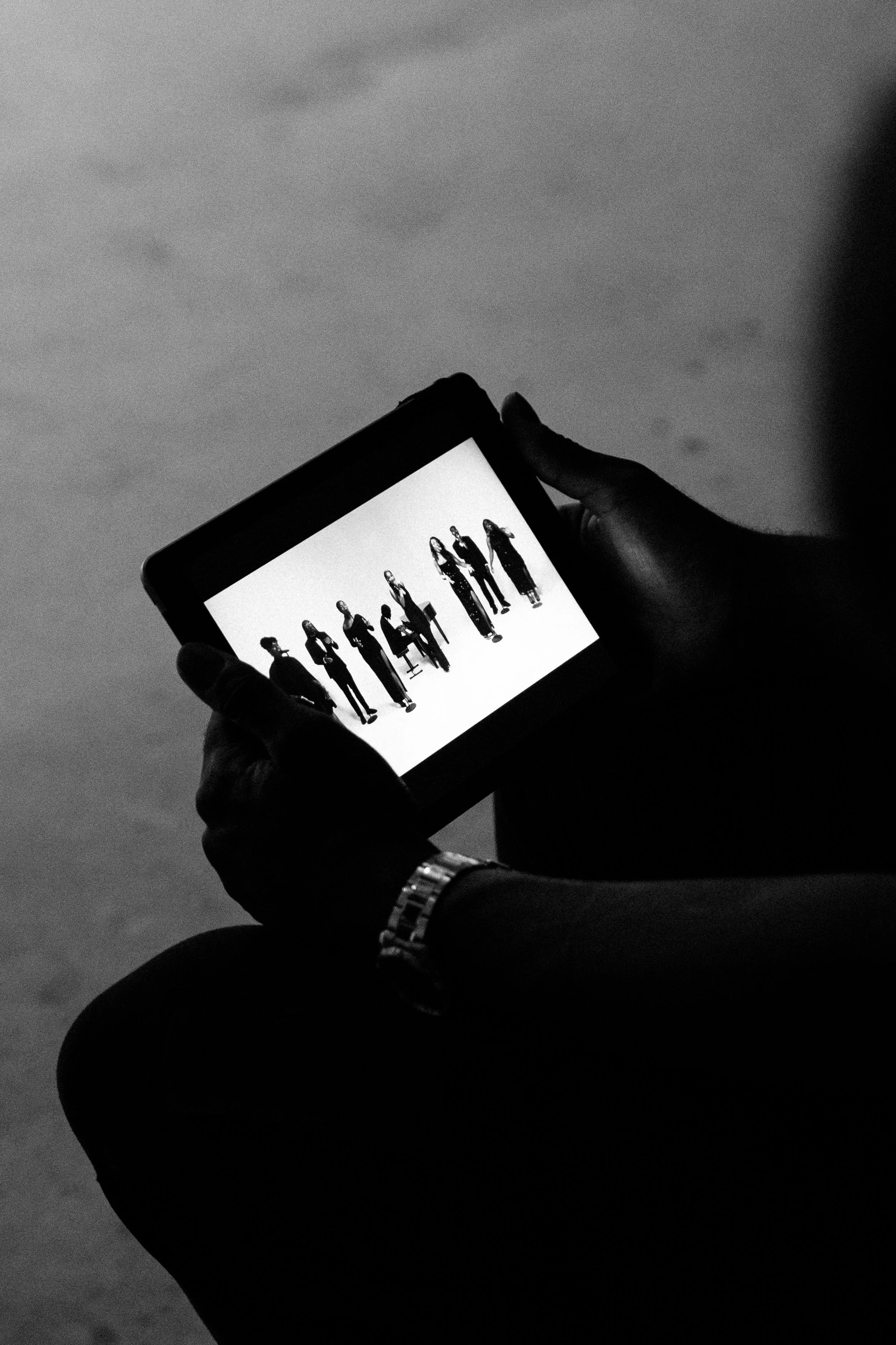 A person holding a tablet displaying a black and white image of eight women standing in a row.