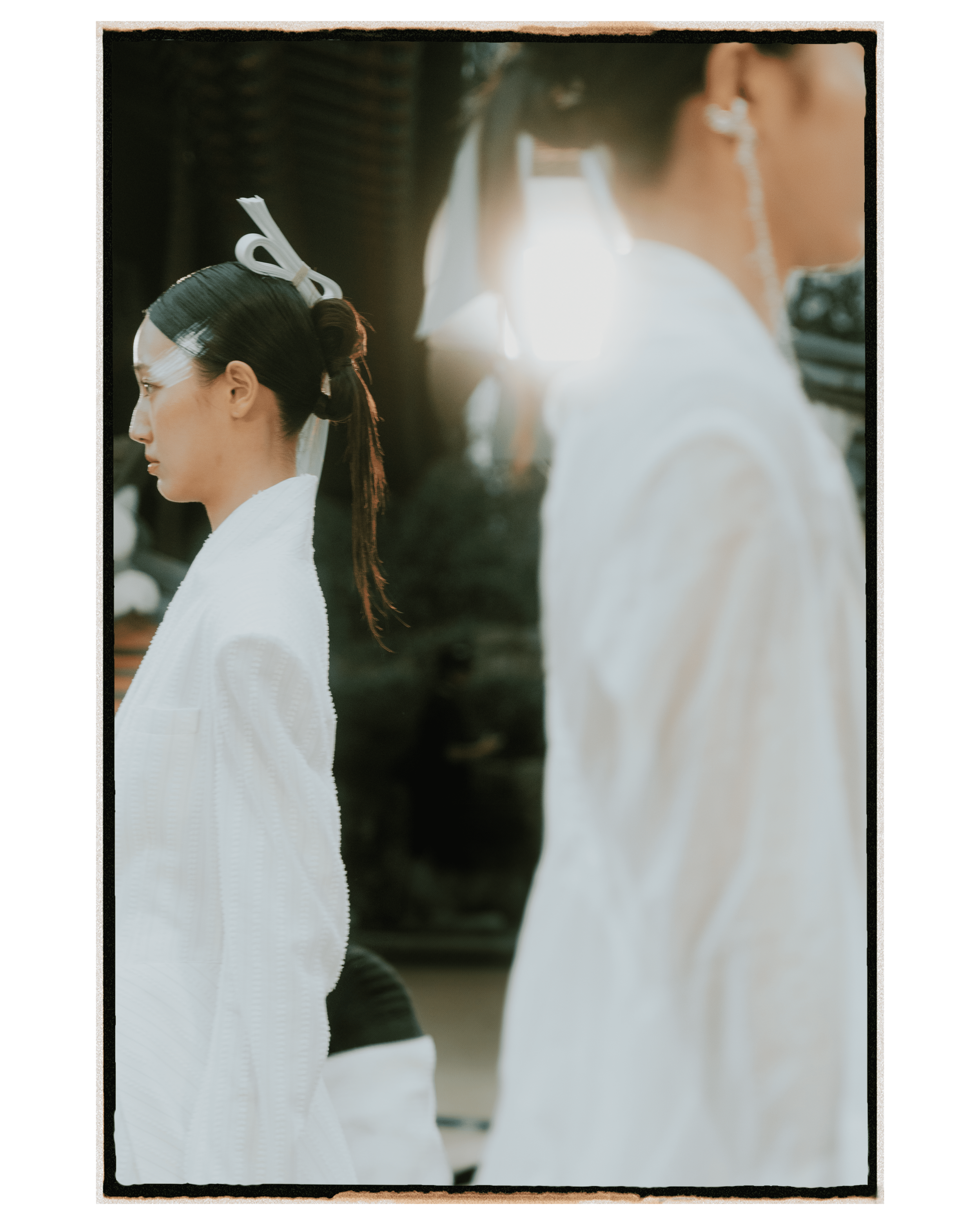 Two women with traditional hairstyles and white kimonos, possibly in a cultural or ceremonial setting.