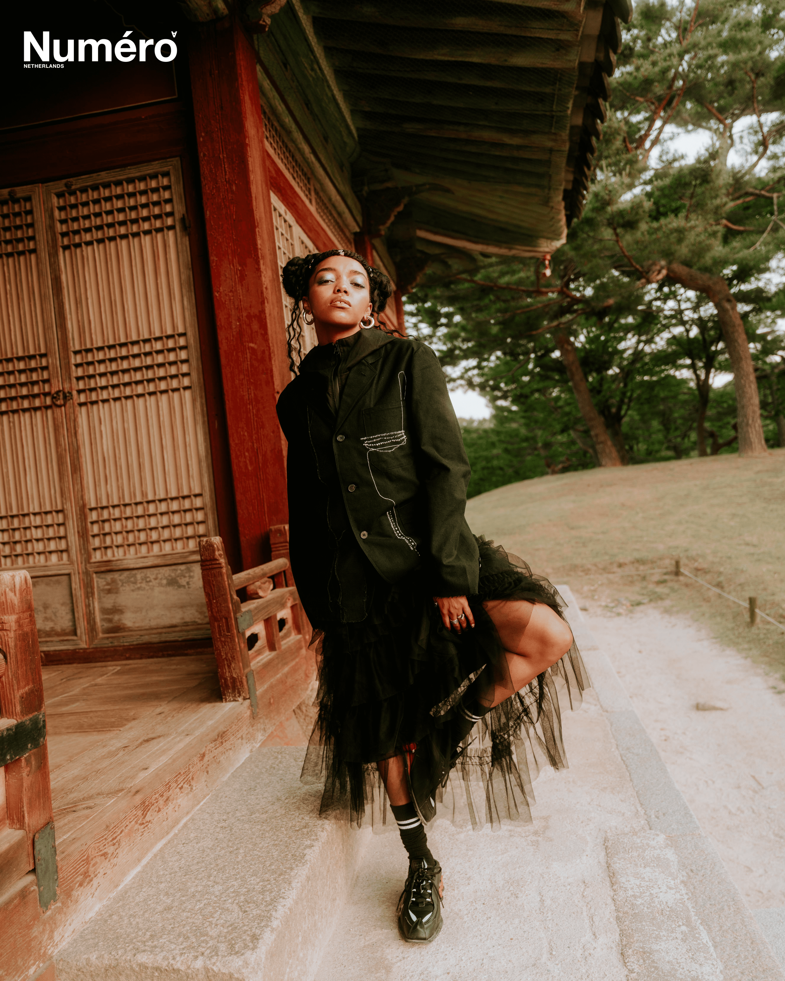 A woman standing on a stone step outside a traditional wooden building with an Asian architectural style, surrounded by trees.