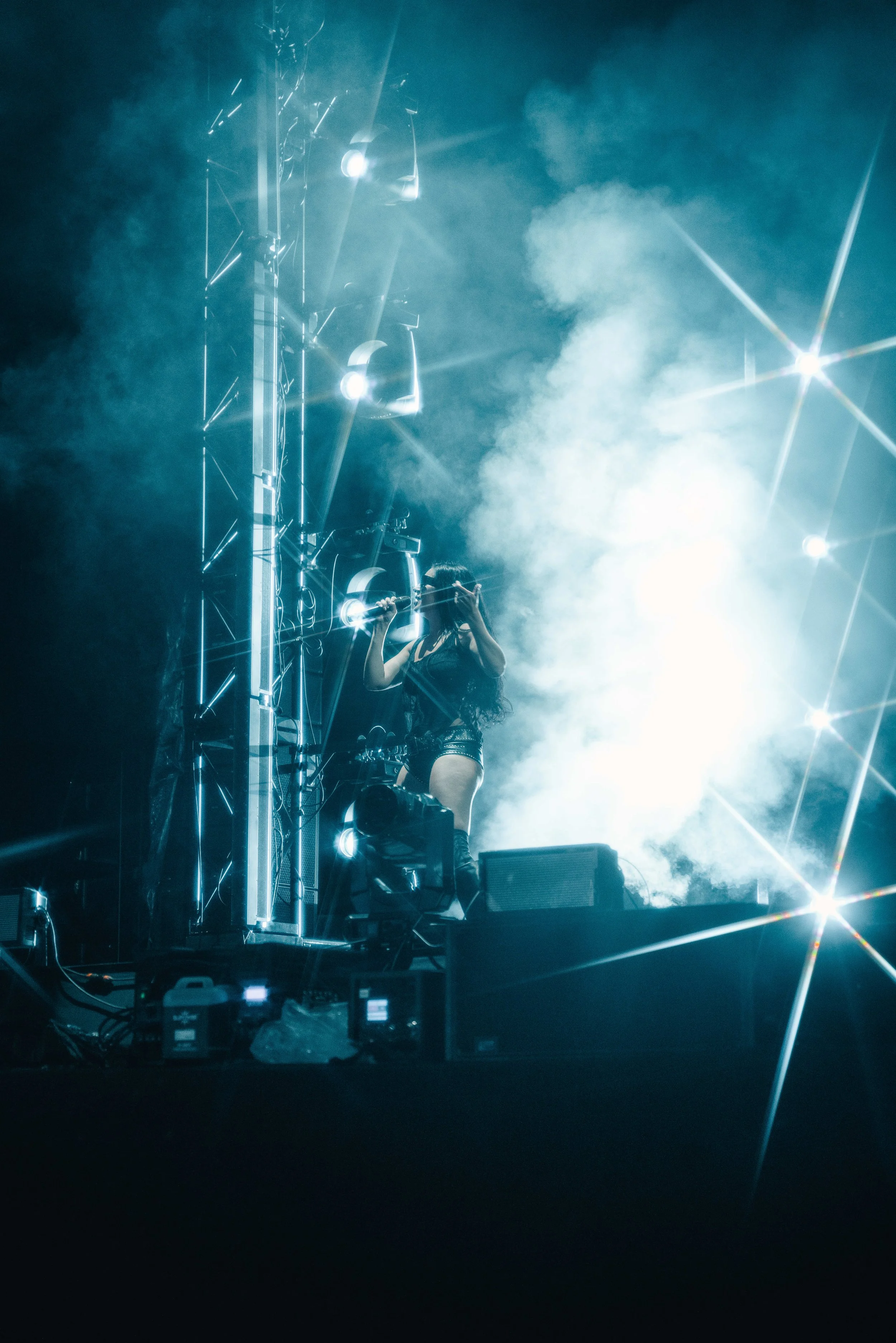 A female DJ is performing on stage with bright white lights, fog, and smoke effects surrounding her.