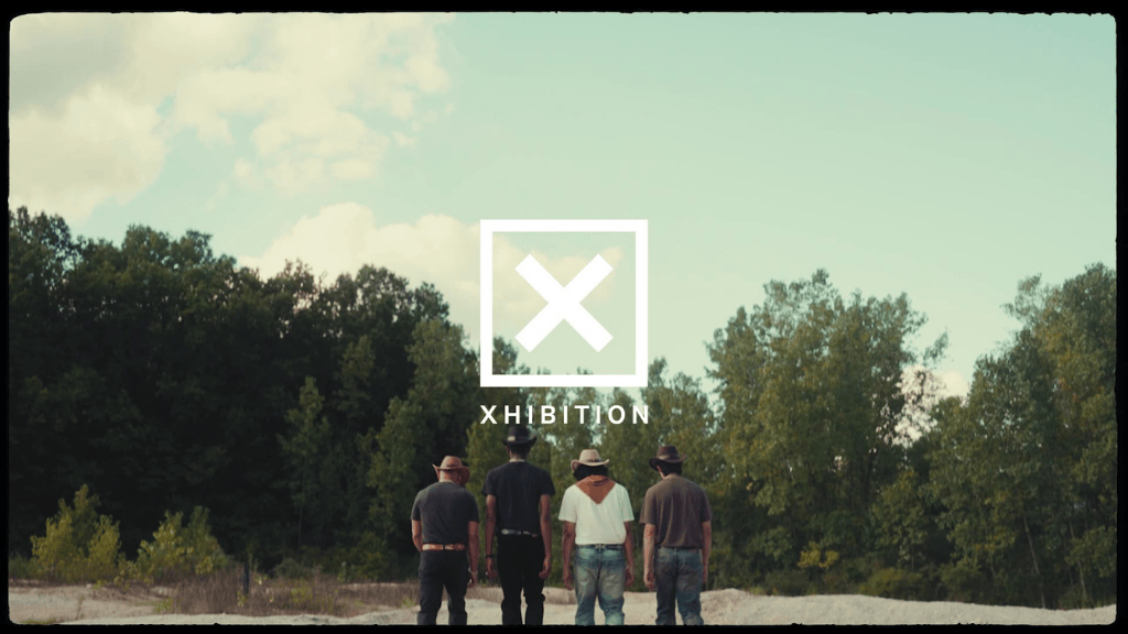 Four people walking away from the camera in an outdoor setting with trees and a cloudy sky in the background, with a logo of a large white 'X' inside a square and the text 'XHIBITION' across the center.