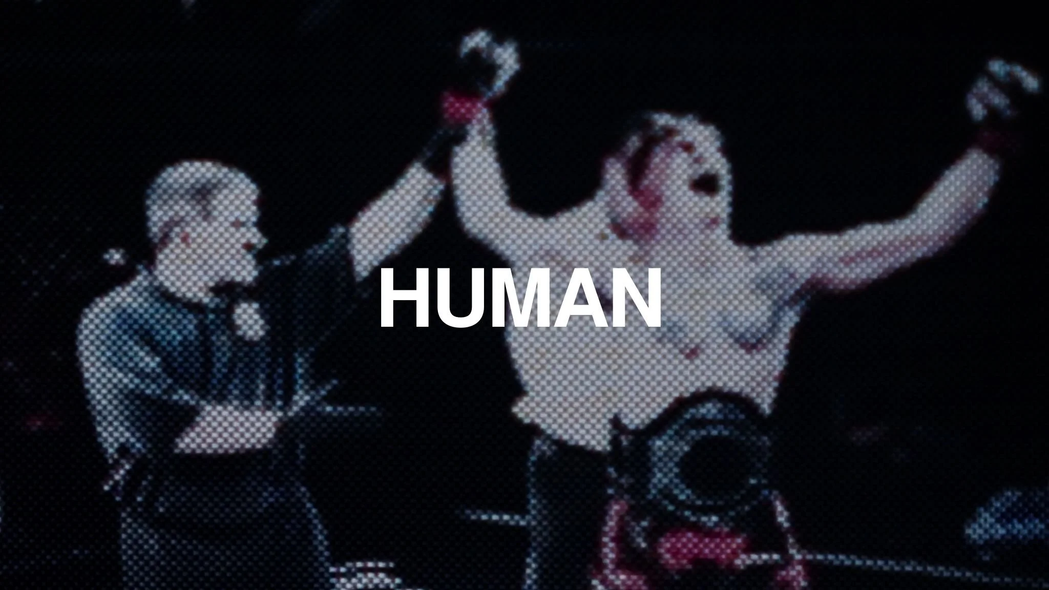 A woman with red hair and black shorts celebrating a victory with her arms raised is accompanied by a woman with short hair and a suit, both on a stage with a dark background.