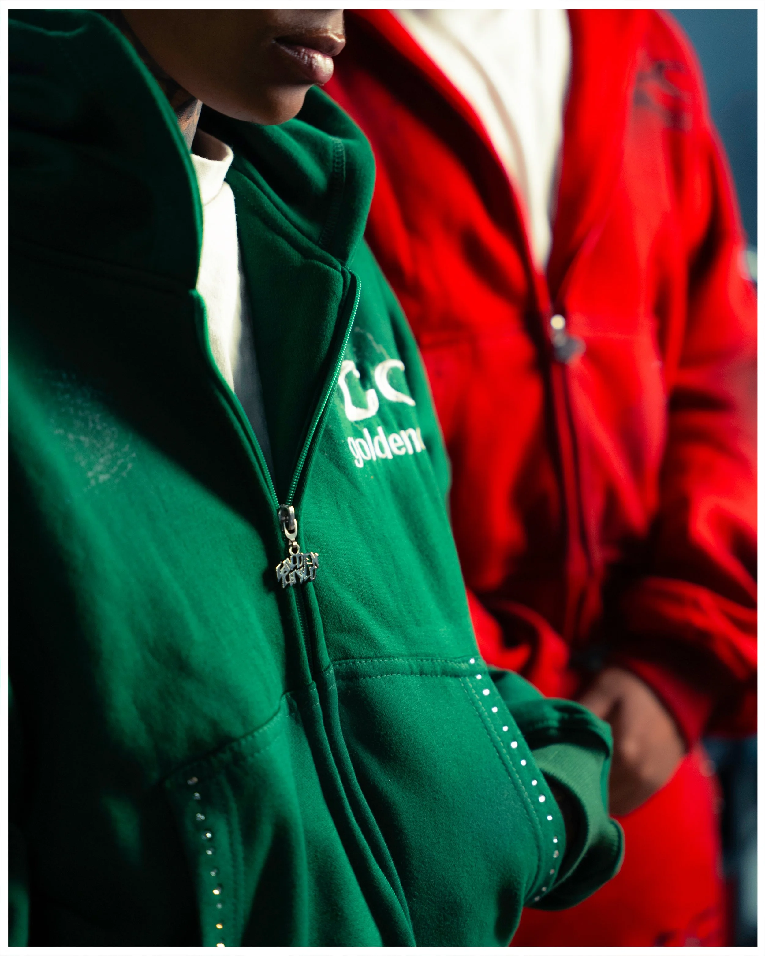 Close-up of two people wearing red and green zip-up jackets, one with the brand 'Golden' visible on the green jacket.