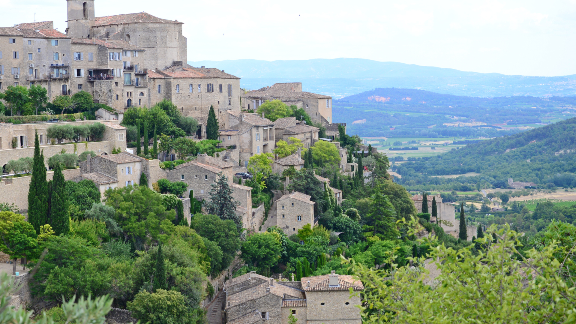 A hillside village with stone buildings and green trees overlooking a valley.