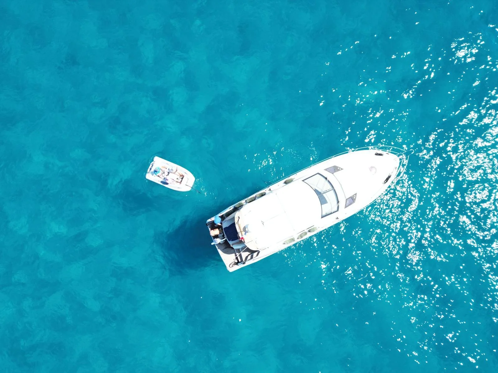 An aerial view of a white yacht and a smaller boat in clear blue water.