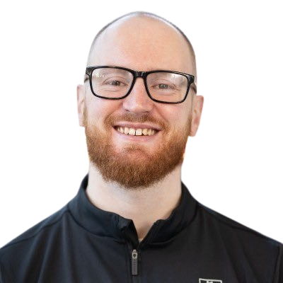 Headshot of a smiling man with glasses, a beard, wearing a black jacket, against a plain background.