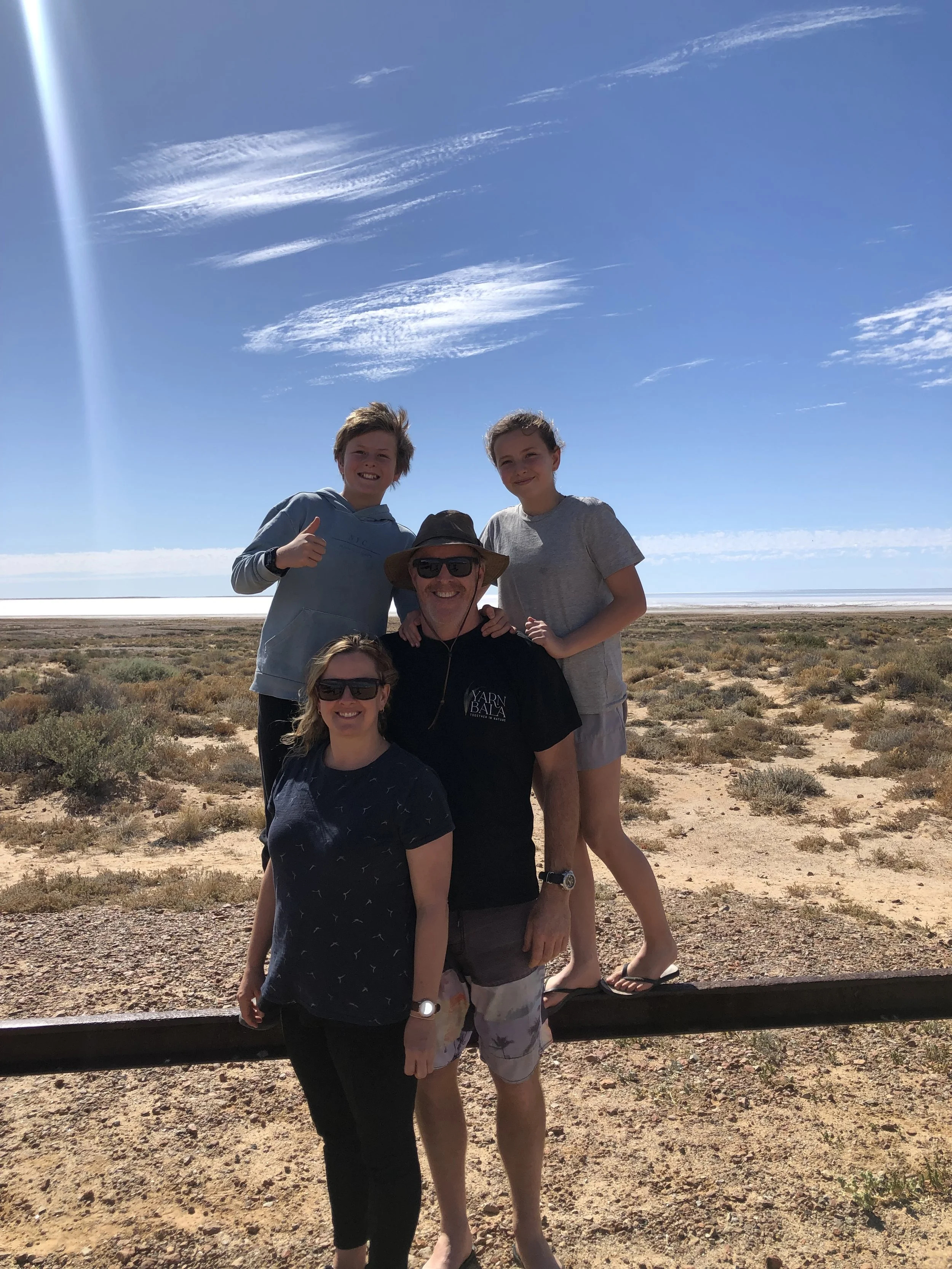 Group of five people standing outdoors in a desert landscape with a blue sky and scattered clouds, posing for a photo.