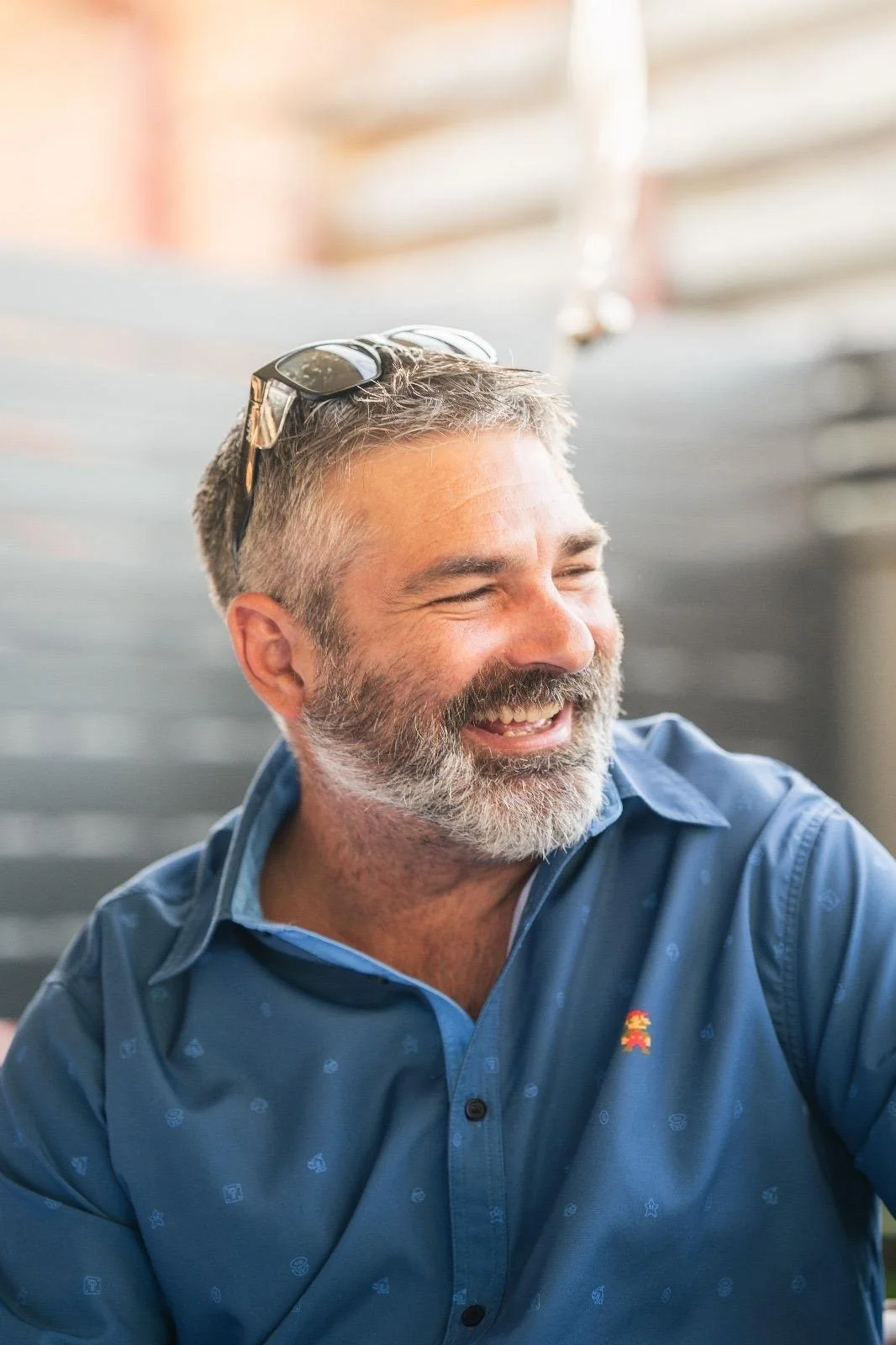 A middle-aged man with gray hair and a beard, smiling and wearing sunglasses on his head, in a casual setting.