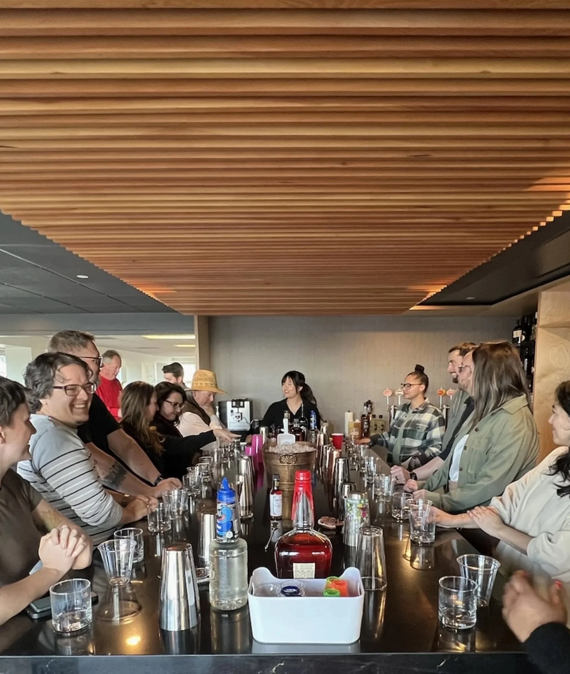 People gathered around a bar table socializing and enjoying drinks in a modern bar setting.