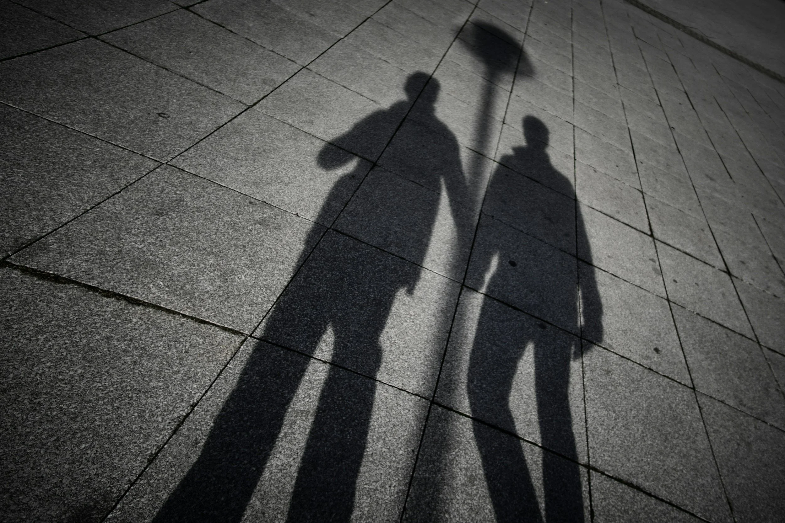 A couple stand holding hands in shadow