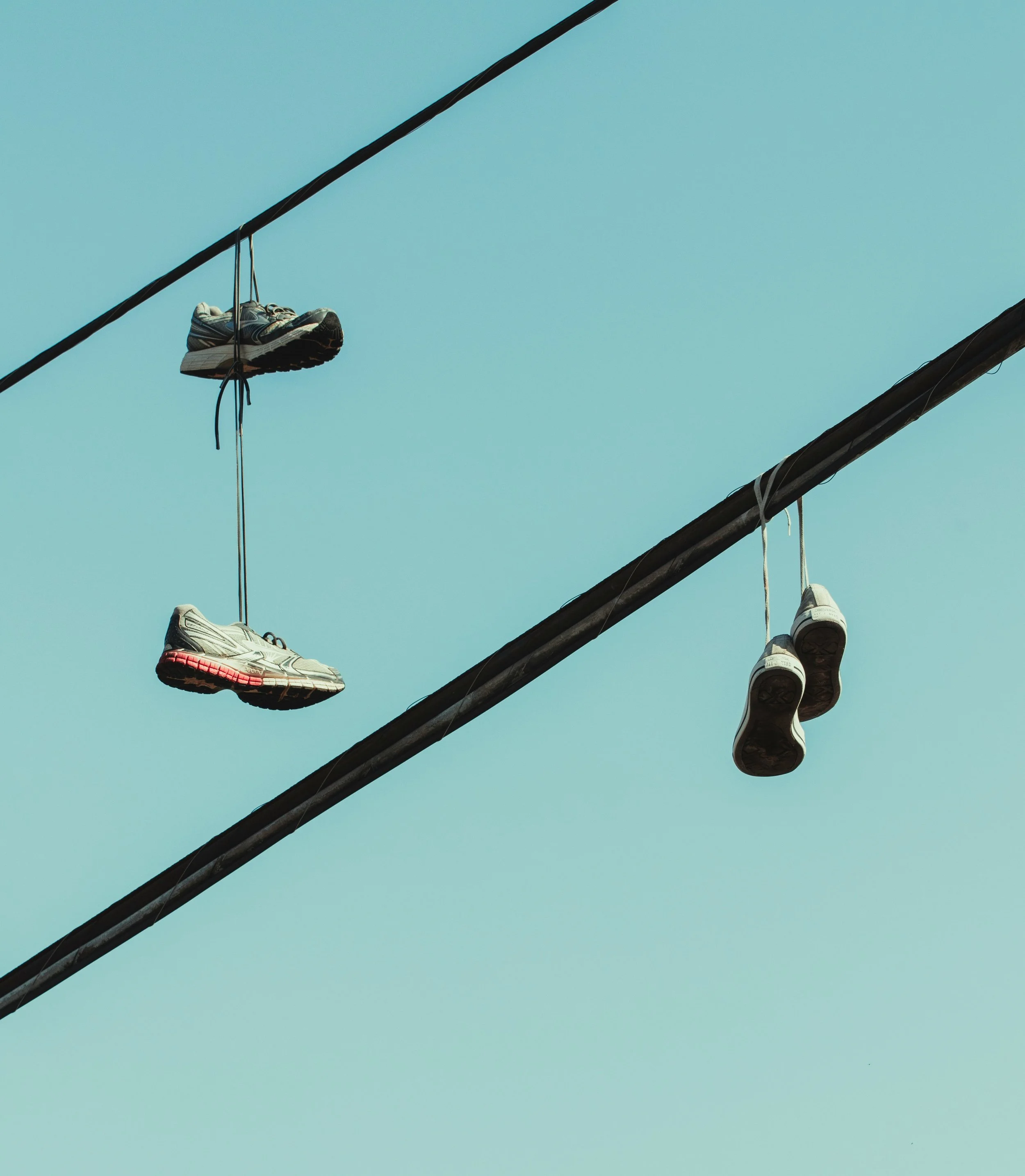 Two pairs of sneakers hanging from power lines against a pale blue sky.