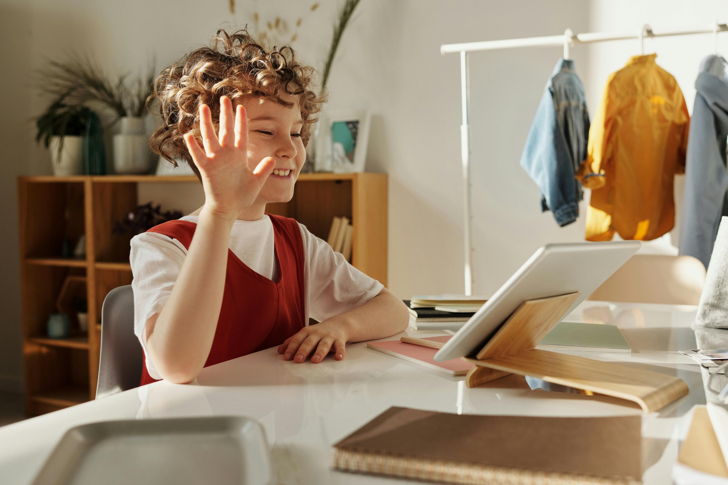 A boy smiles and waves during an online tutoring session