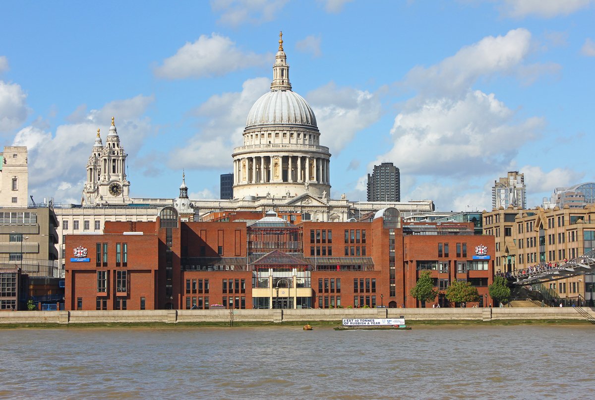 View of St. Paul's Cathedral in London from across the River Thames, with modern and historic buildings in the foreground and partly cloudy skies overhead.