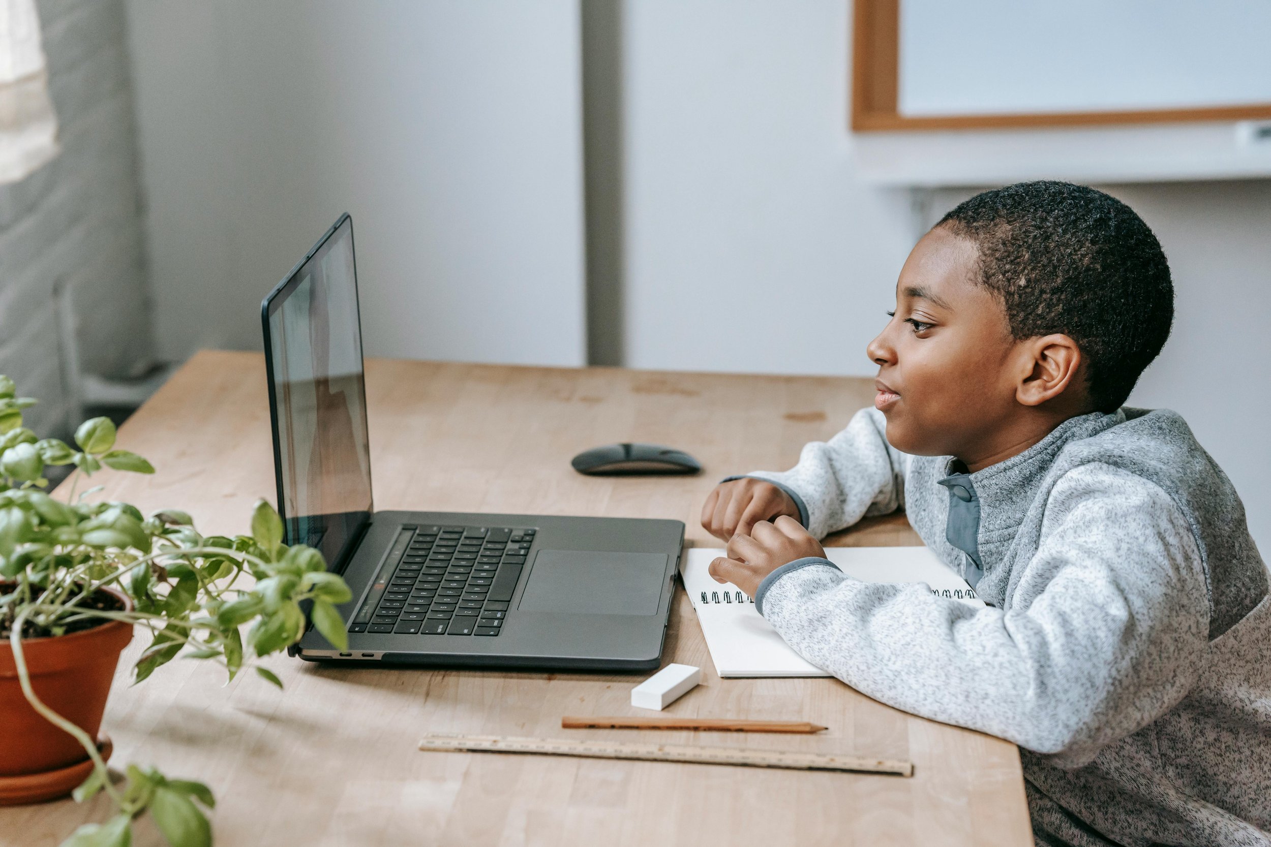 A young boy engaged in an online lesson on a laptop at a wooden desk.
