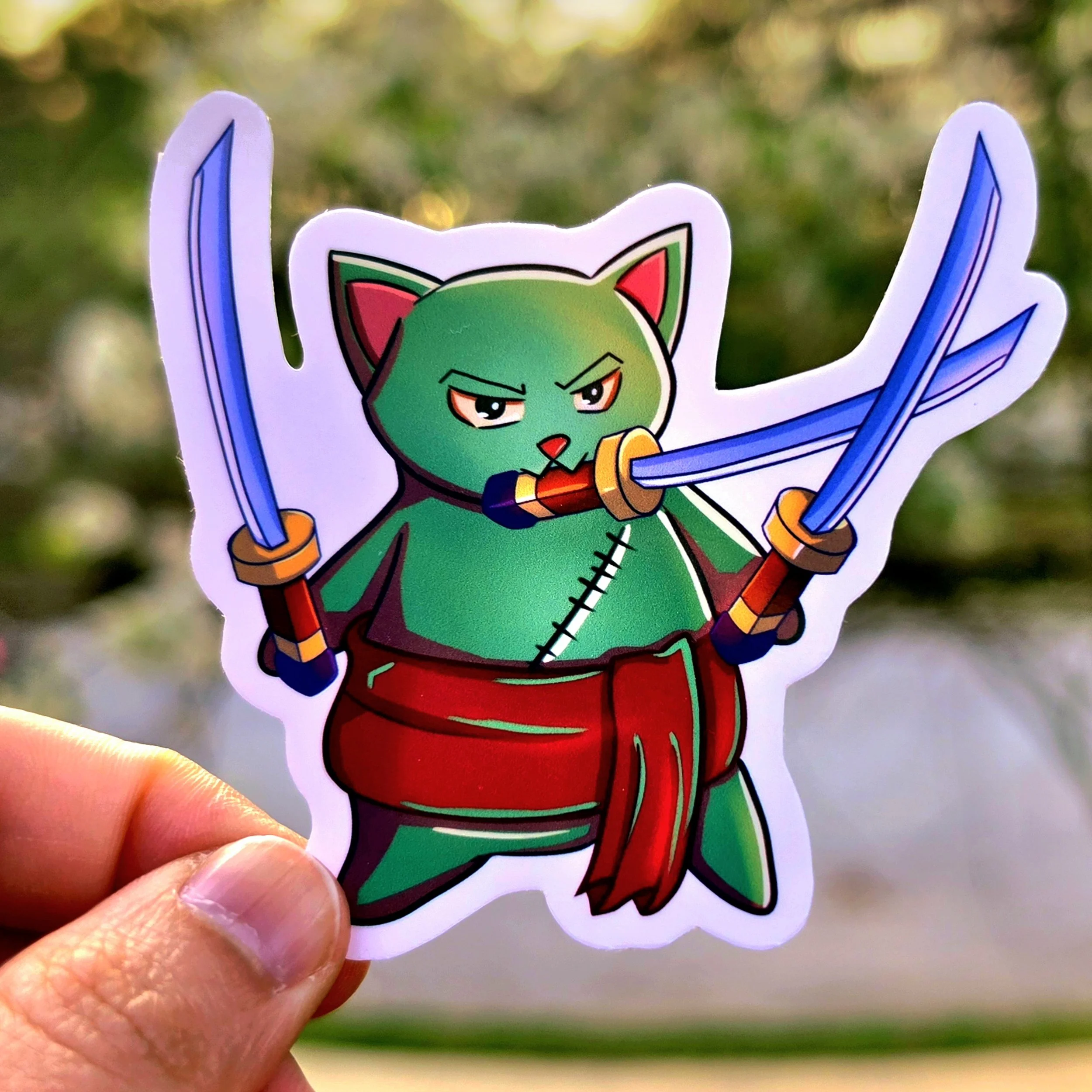 The Swordsman (Zoro): A physical die-cut sticker featuring a stoic green-furred cat inspired by Roronoa Zoro. The feline holds three katanas—one in its mouth and two in its paws