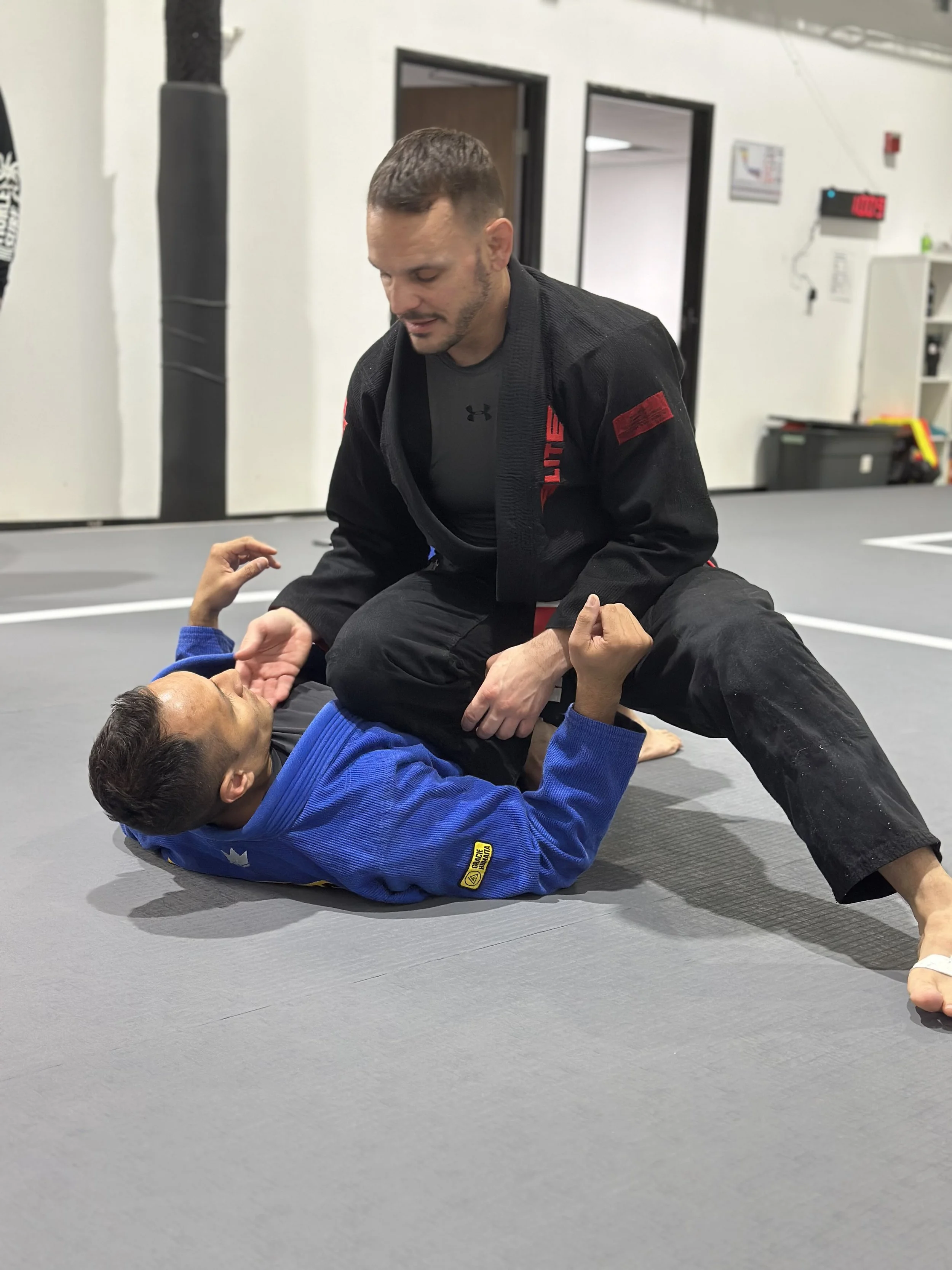 Close-up of a person in a white martial arts gi sitting on a wooden bench, with their hand resting on their lap and holding white belt straps.