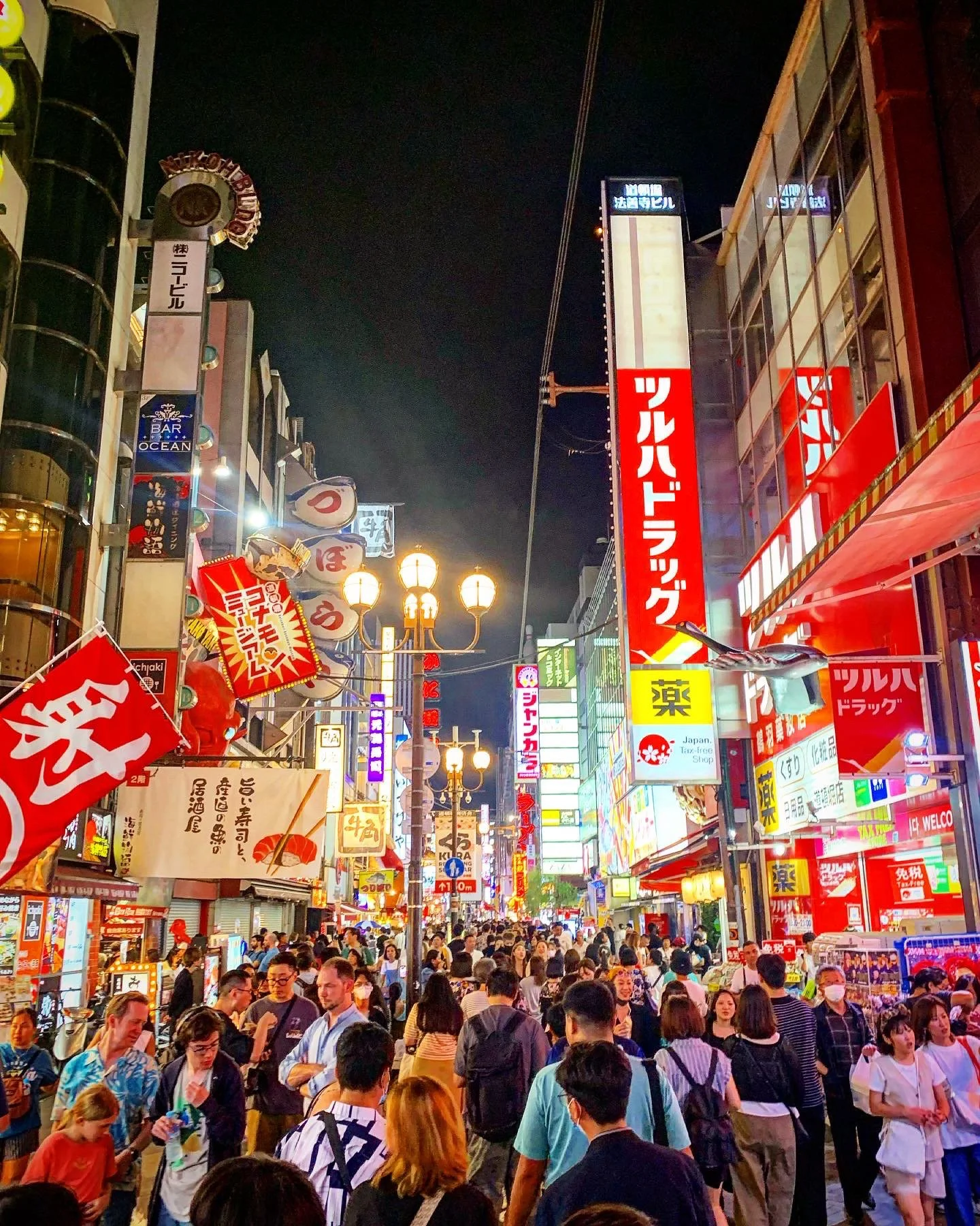 Busy street in Japan with illuminated shopfronts, signs and pedestrians at night.