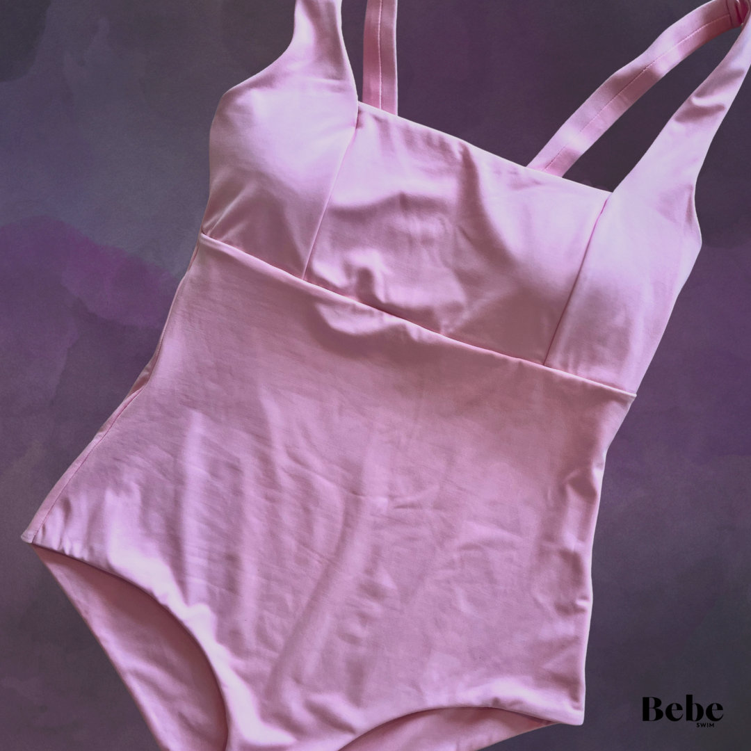 A pink womens swimsuit with a supportive top and full brief bottom, laid flat on a dark purple background.
