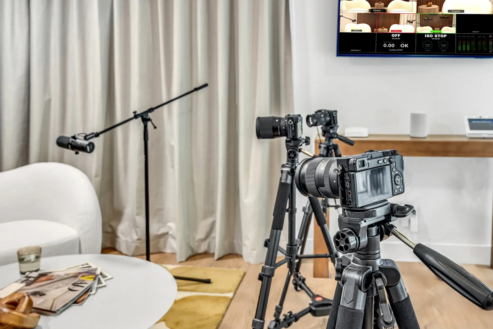 Camera equipment and boom microphone in the Light Studio at Venice Podcast Studio, Los Angeles, with white interview seating and neutral curtain backdrop