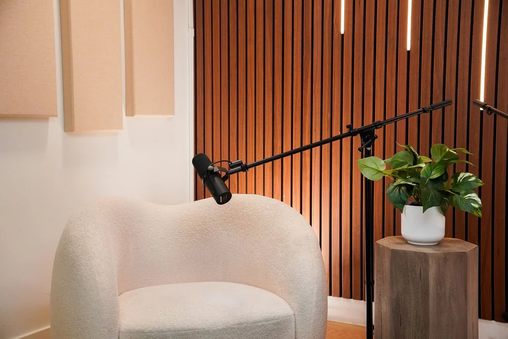 Cream bouclé lounge chair and microphone stand against a wood slat wall with plant accent in the Copenhagen set at Venice Podcast Studio