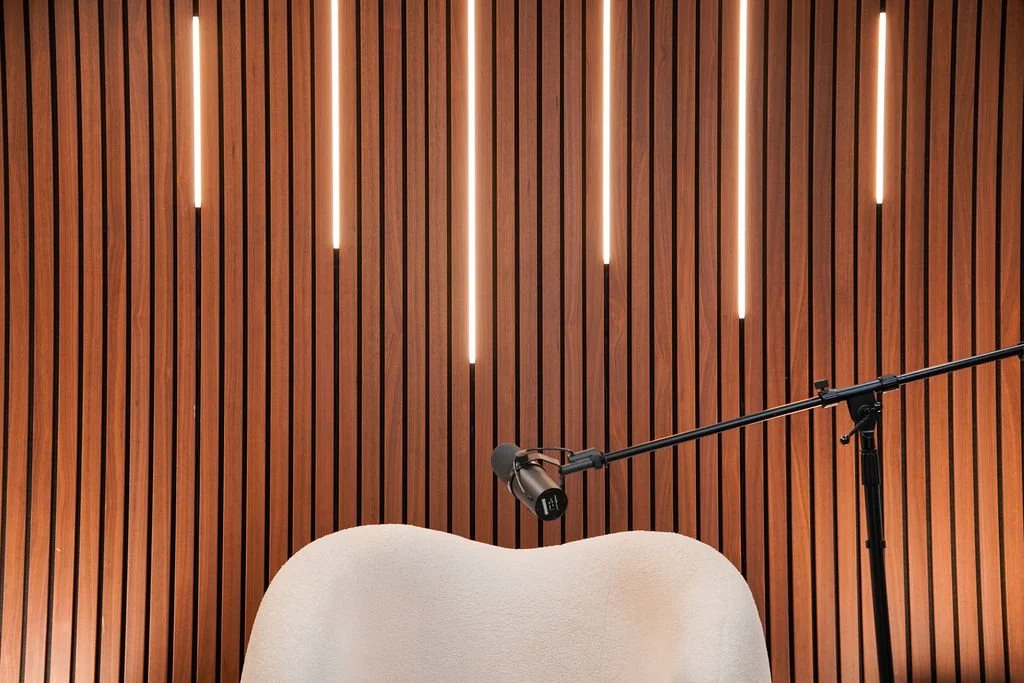 Close-up of a cream bouclé lounge chair with microphone boom arm against an illuminated wood slat wall with LED lighting