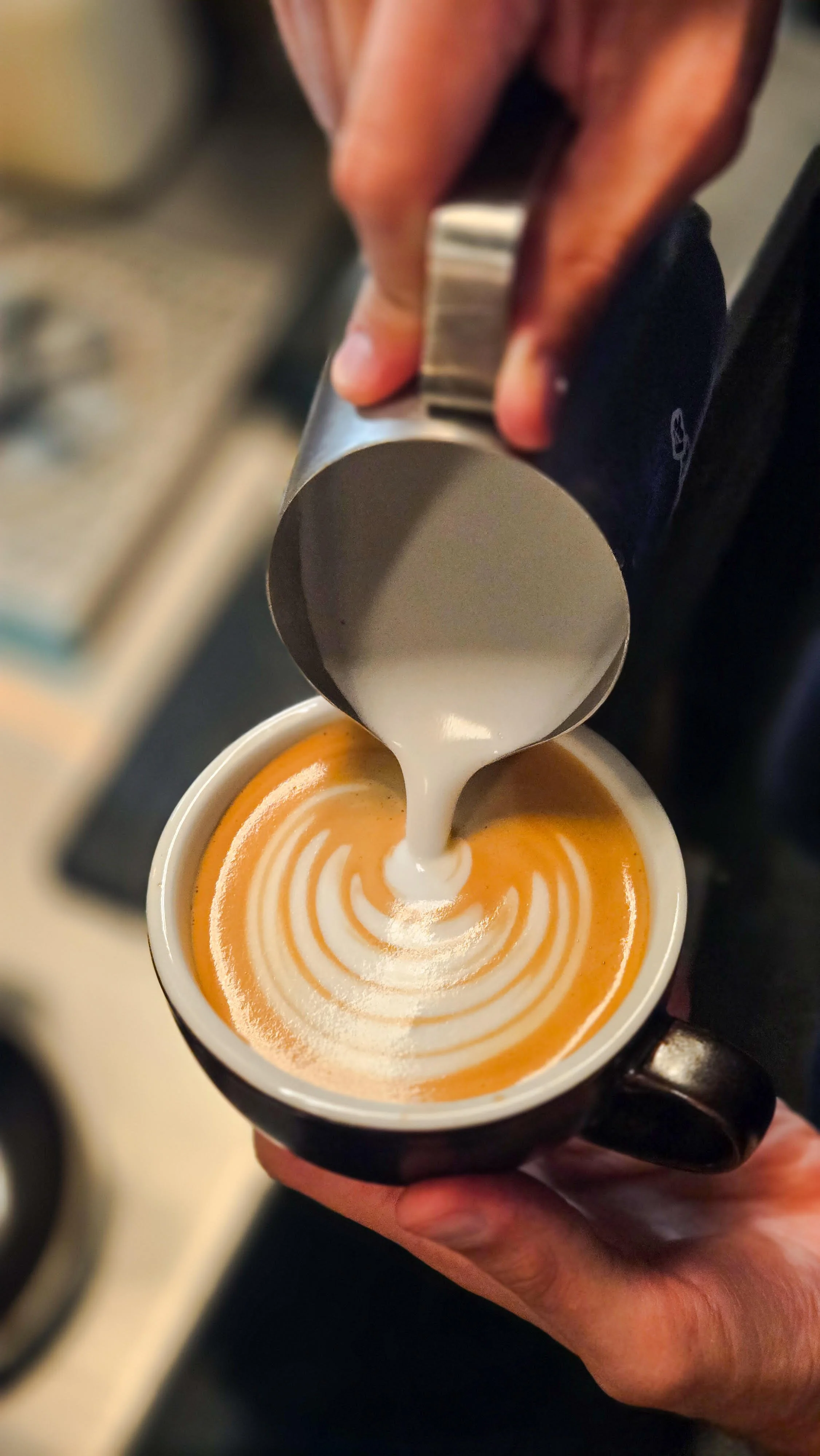 Barista pouring steamed milk into a cup of espresso to create latte art.