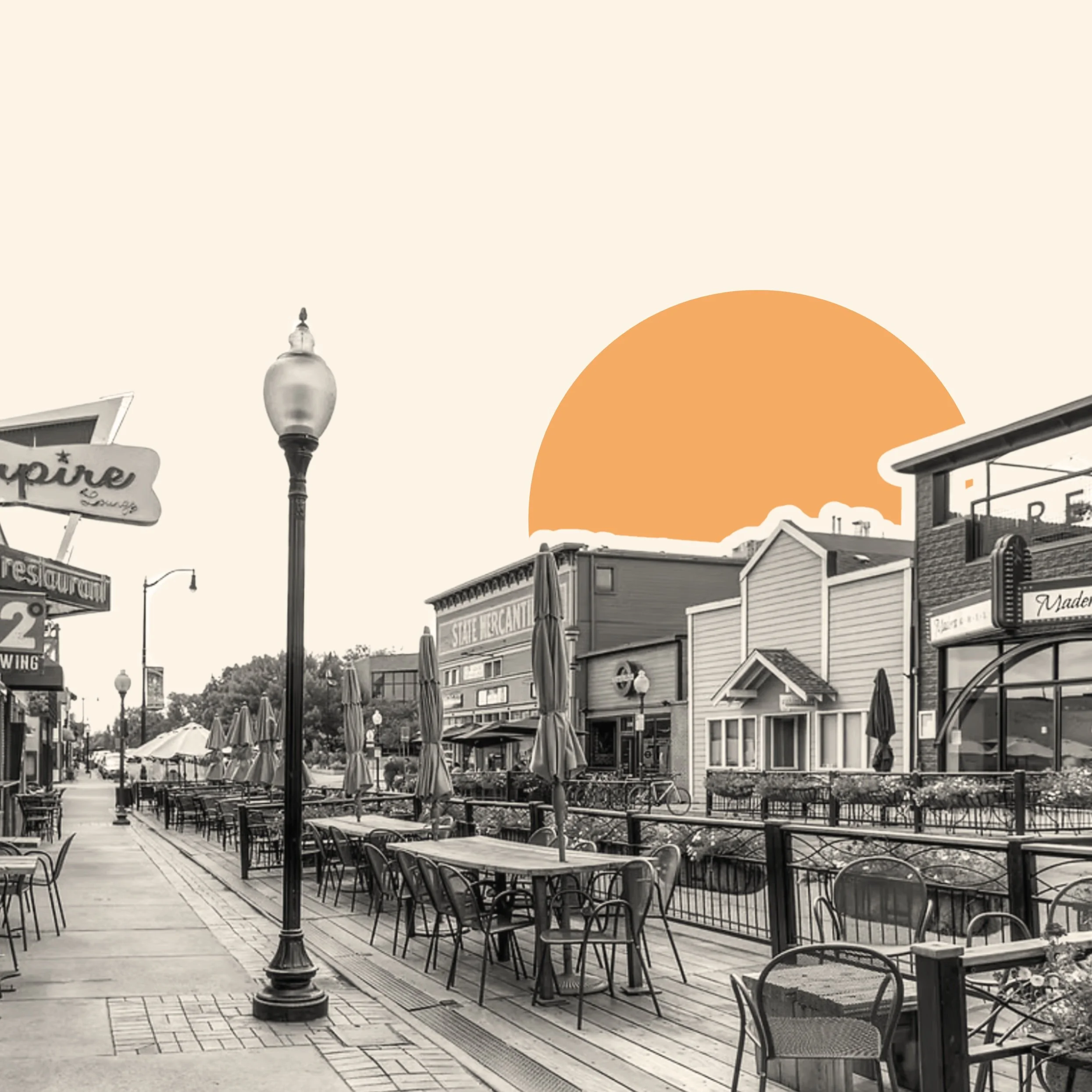 Empty outdoor café seating area on a boardwalk with tables, chairs, and umbrellas, beside shops and businesses, with an orange semi-circle in the sky.