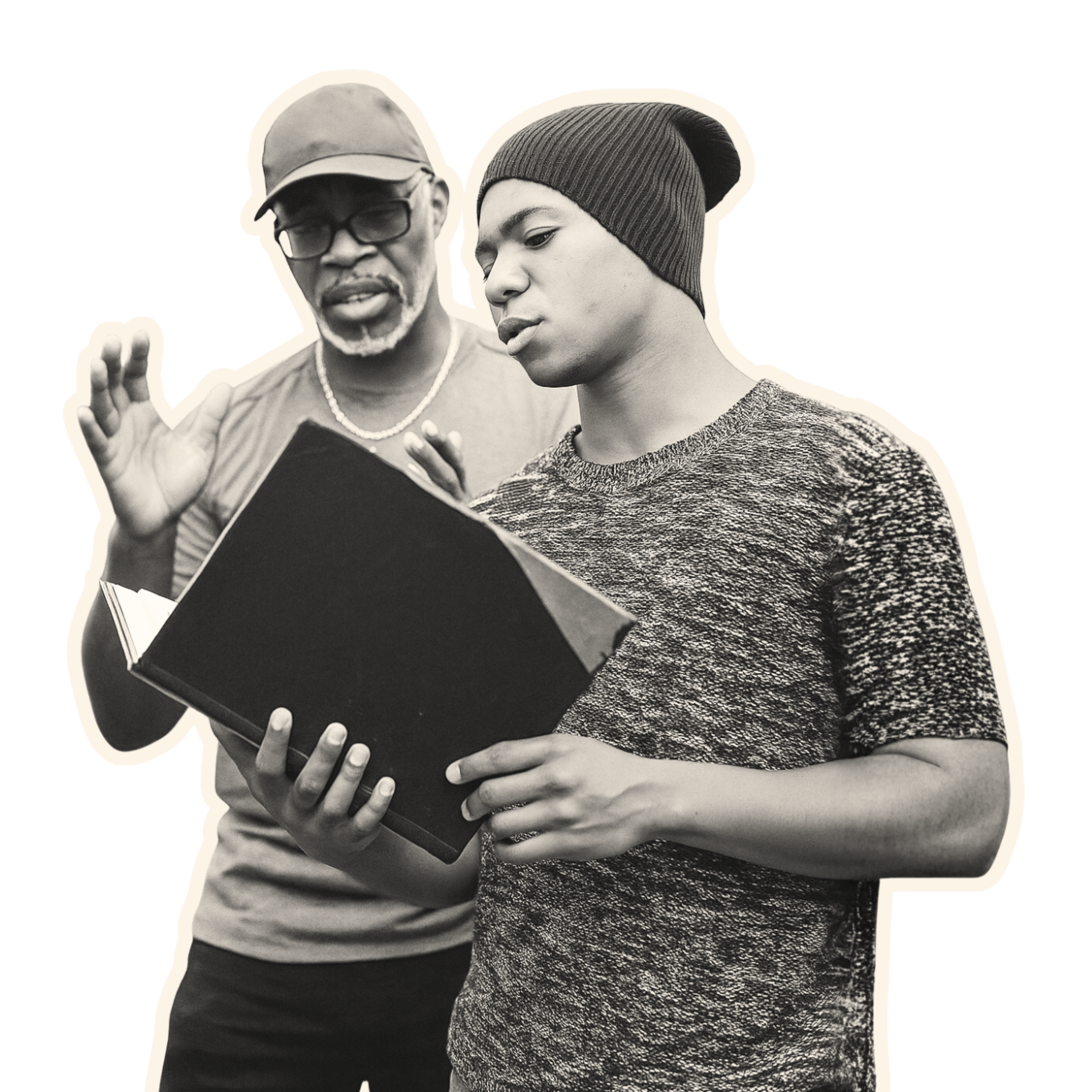 An older man with glasses and a beard explaining something to a young man with a beanie hat, both looking at a book.